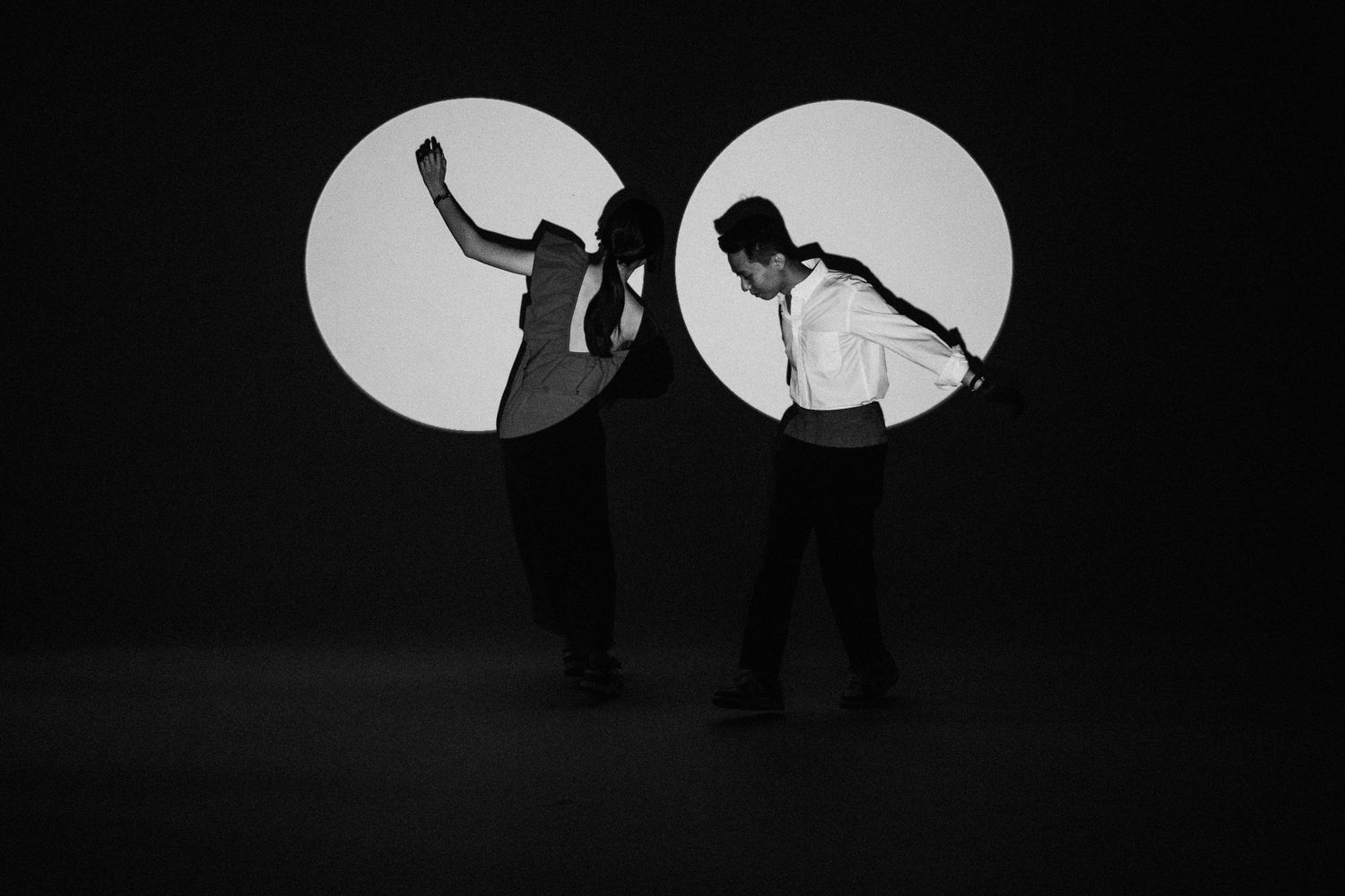 Two figures appear as silhouettes dancing in a spotlight against a dark background.