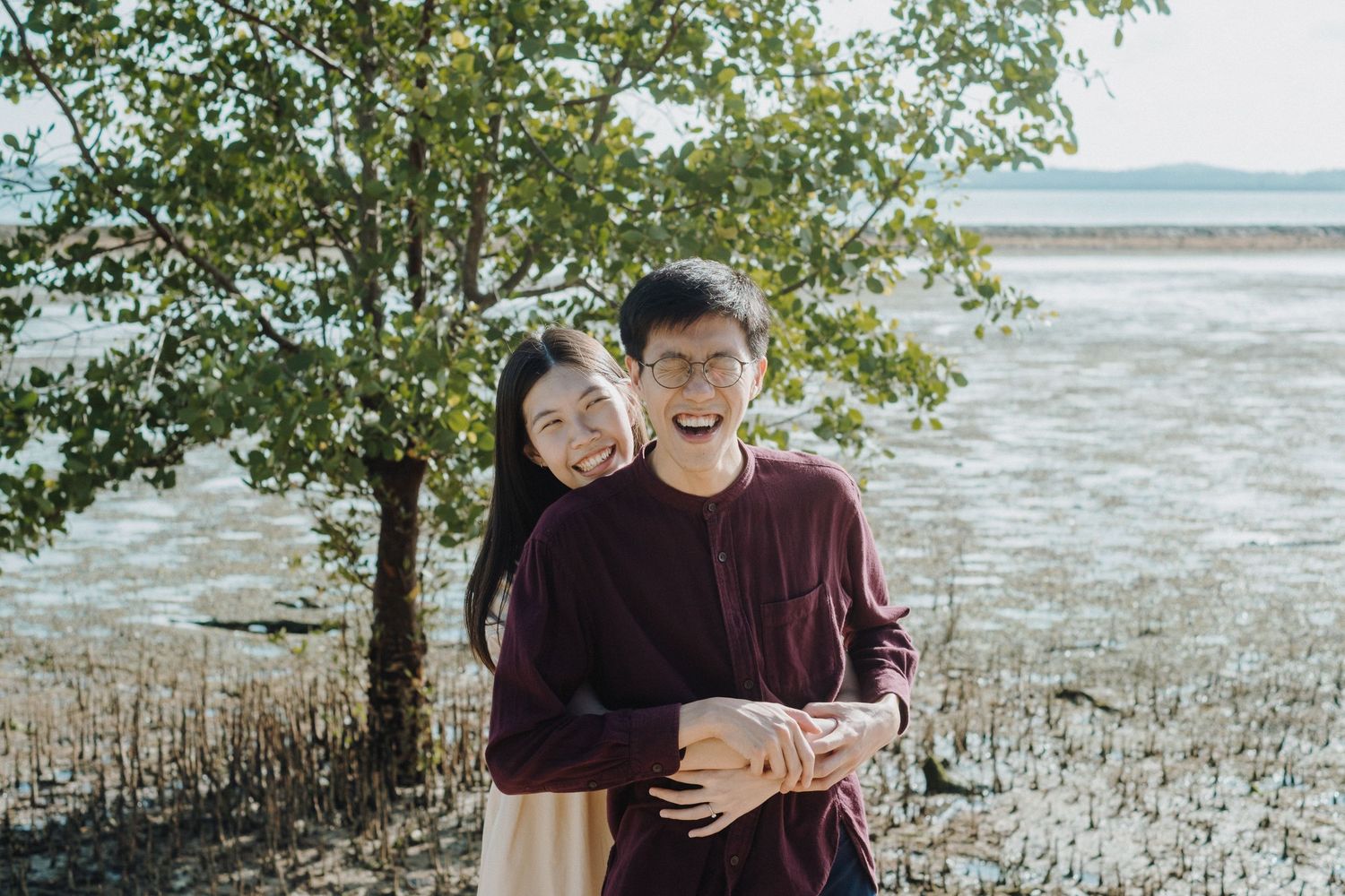 Couple embracing near mangrove trees along a scenic coastal shoreline.
