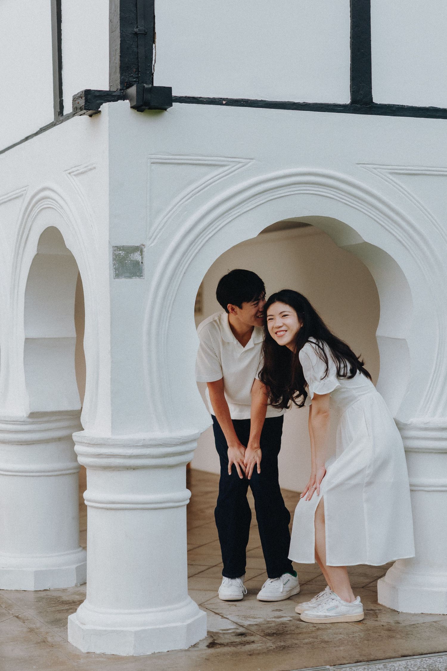 A couple sharing a joyful moment together while posing in white archways of a building.