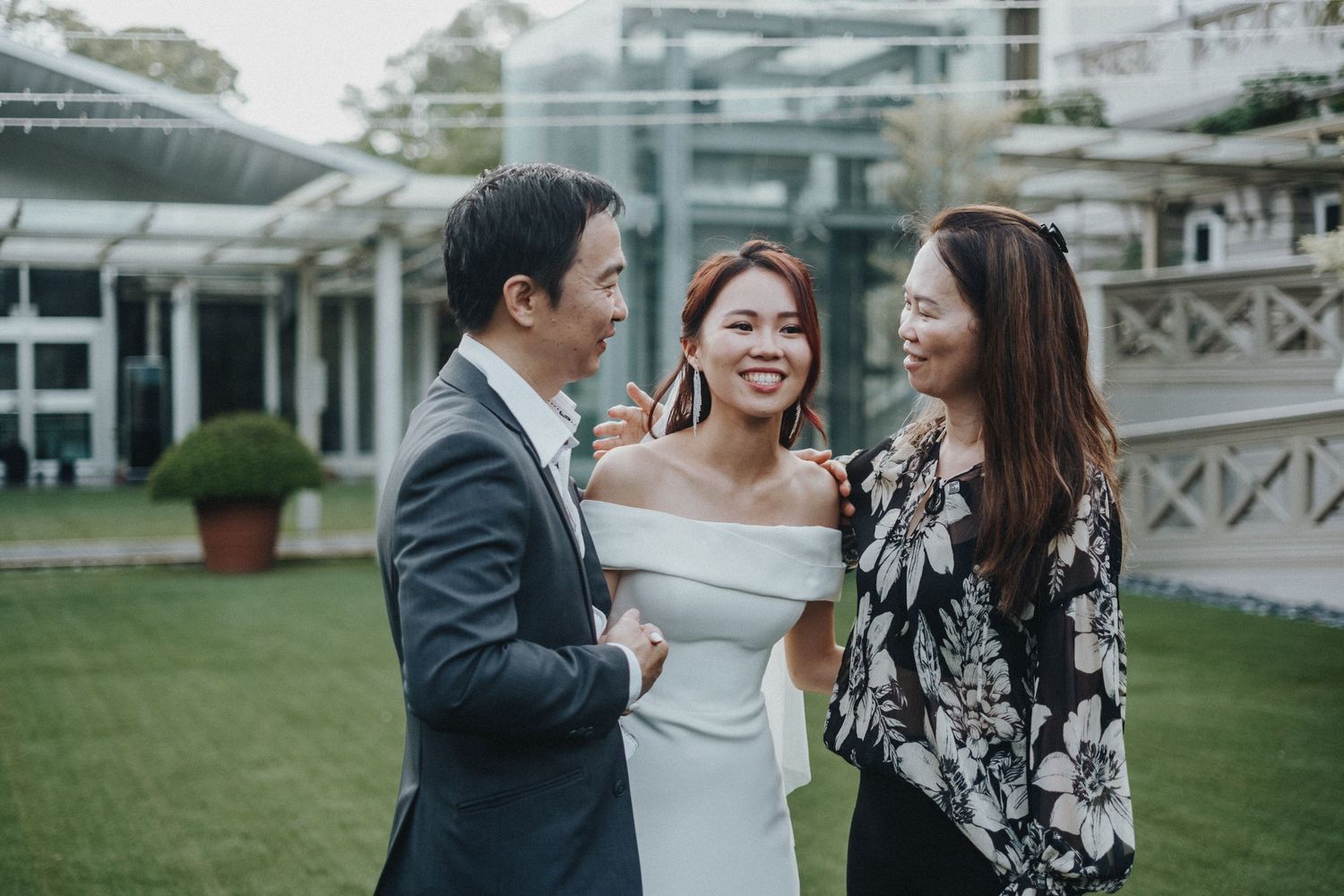 Three friends sharing a joyful moment on a green lawn with white architectural structures in the background.
