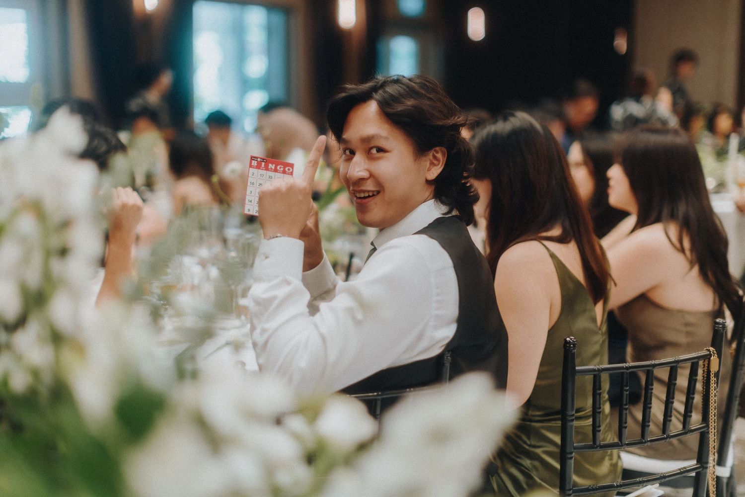 Wedding reception guest raises glass in celebration among decorative table settings.