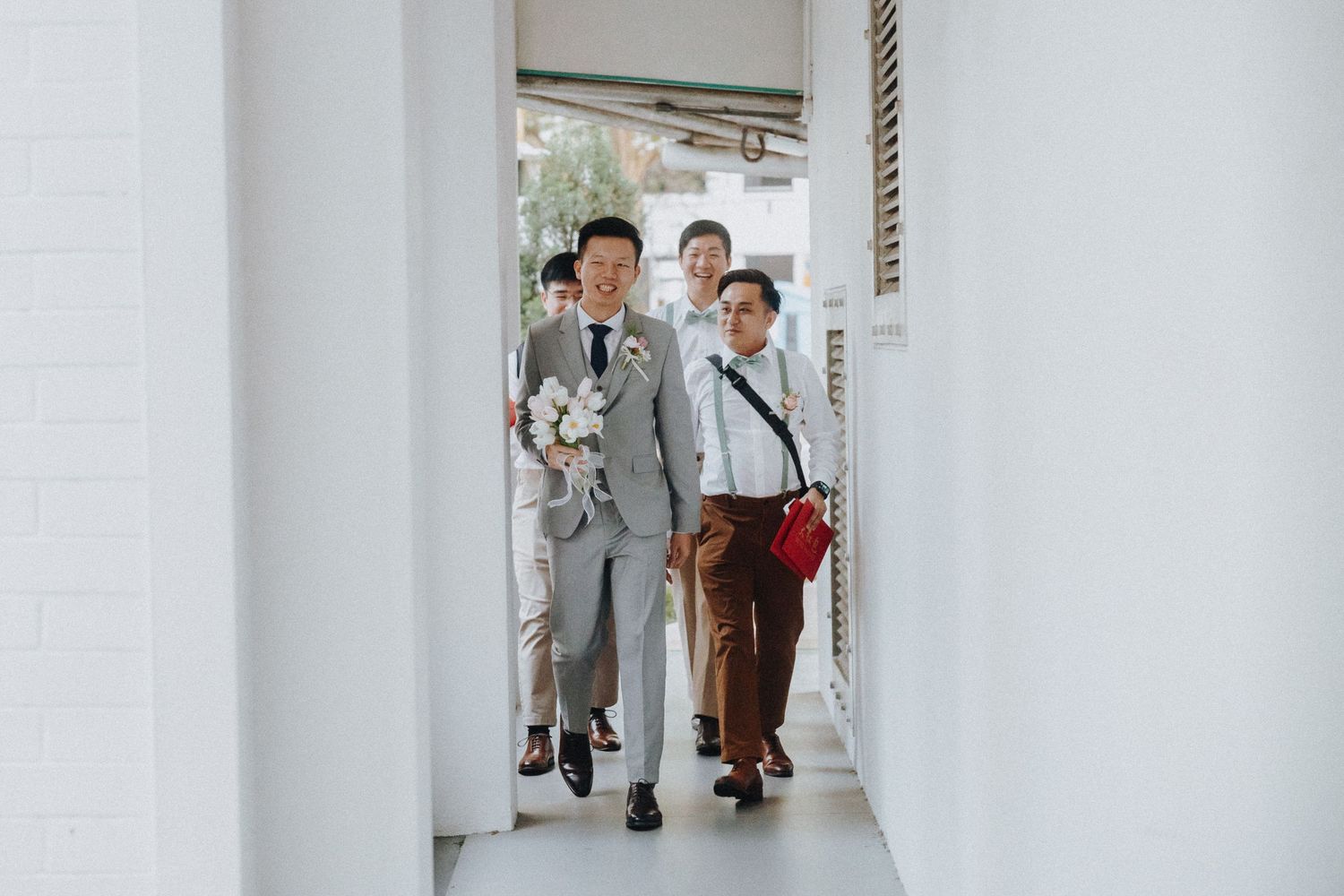 Two people walking together through a bright white hallway with one wearing a grey suit.