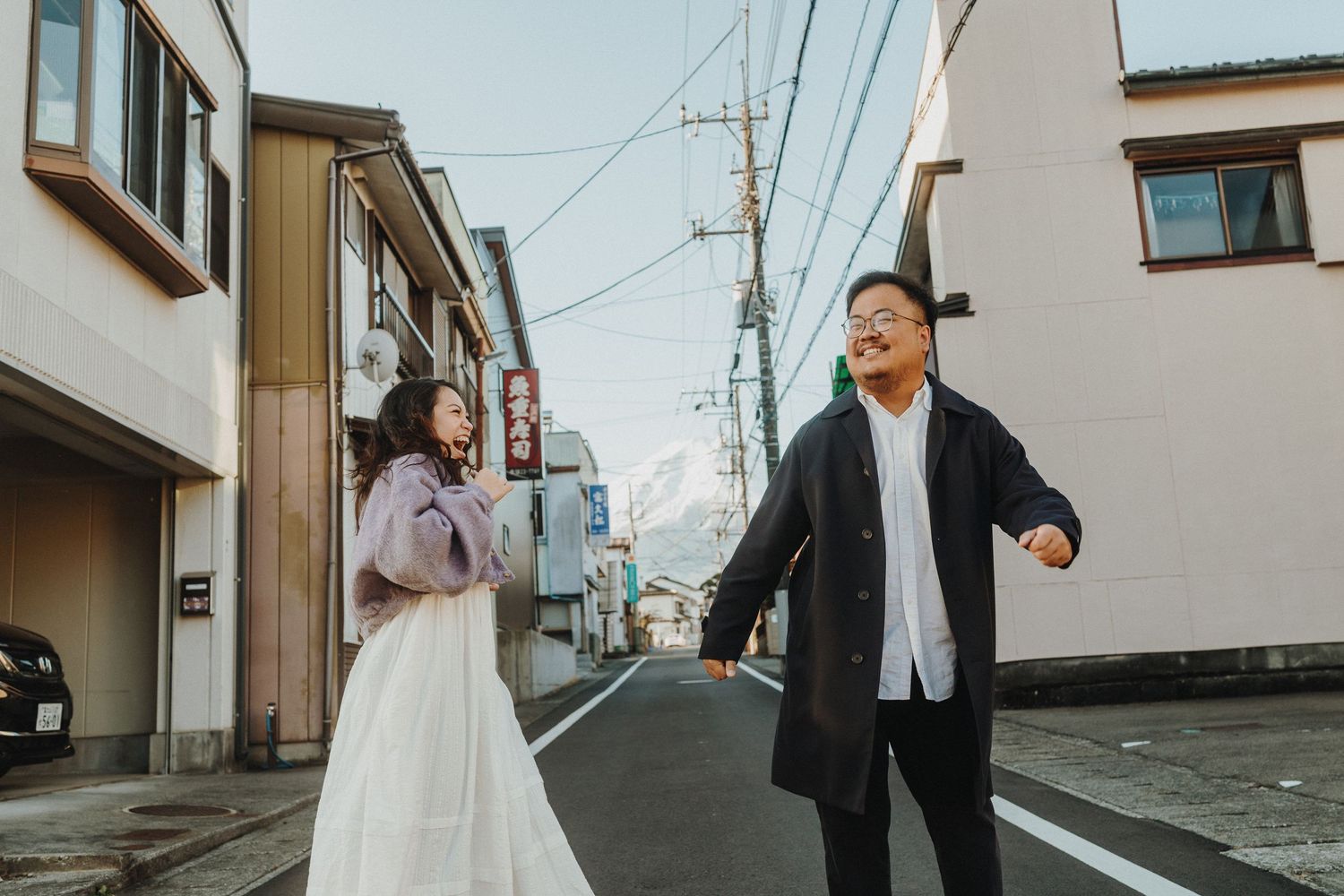 People walking along a residential street in Japan with traditional buildings and power lines.