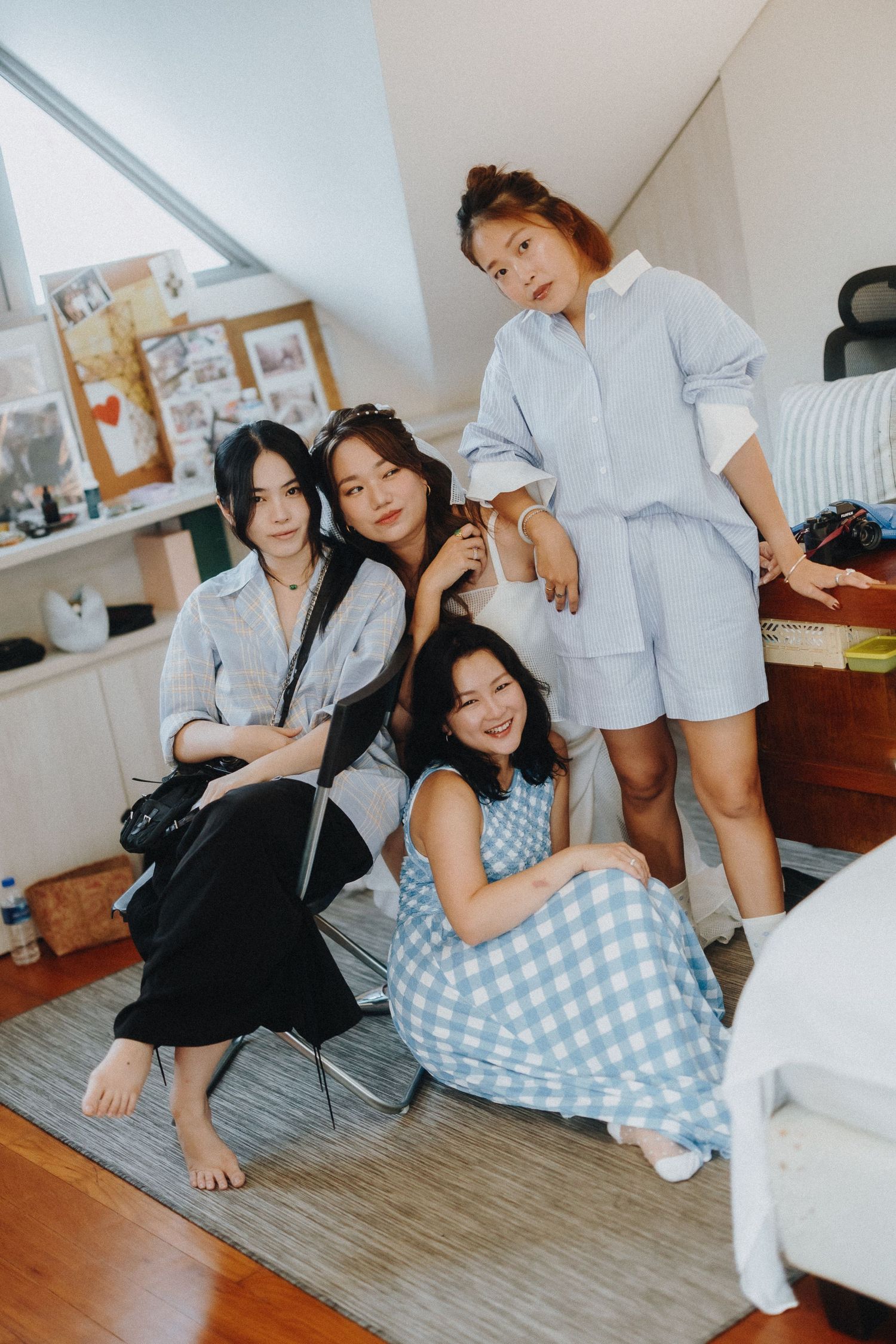 Friends in casual outfits pose together in a cozy bedroom setting.