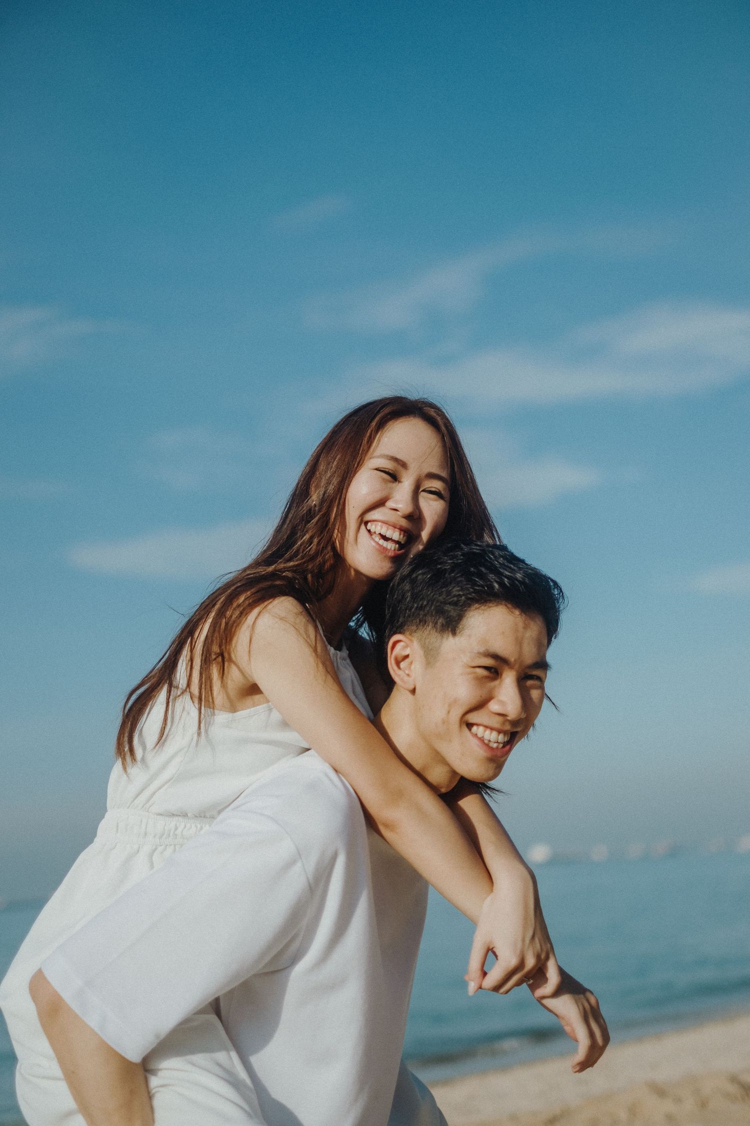 A joyful piggyback ride on the beach with the ocean and blue sky as backdrop.