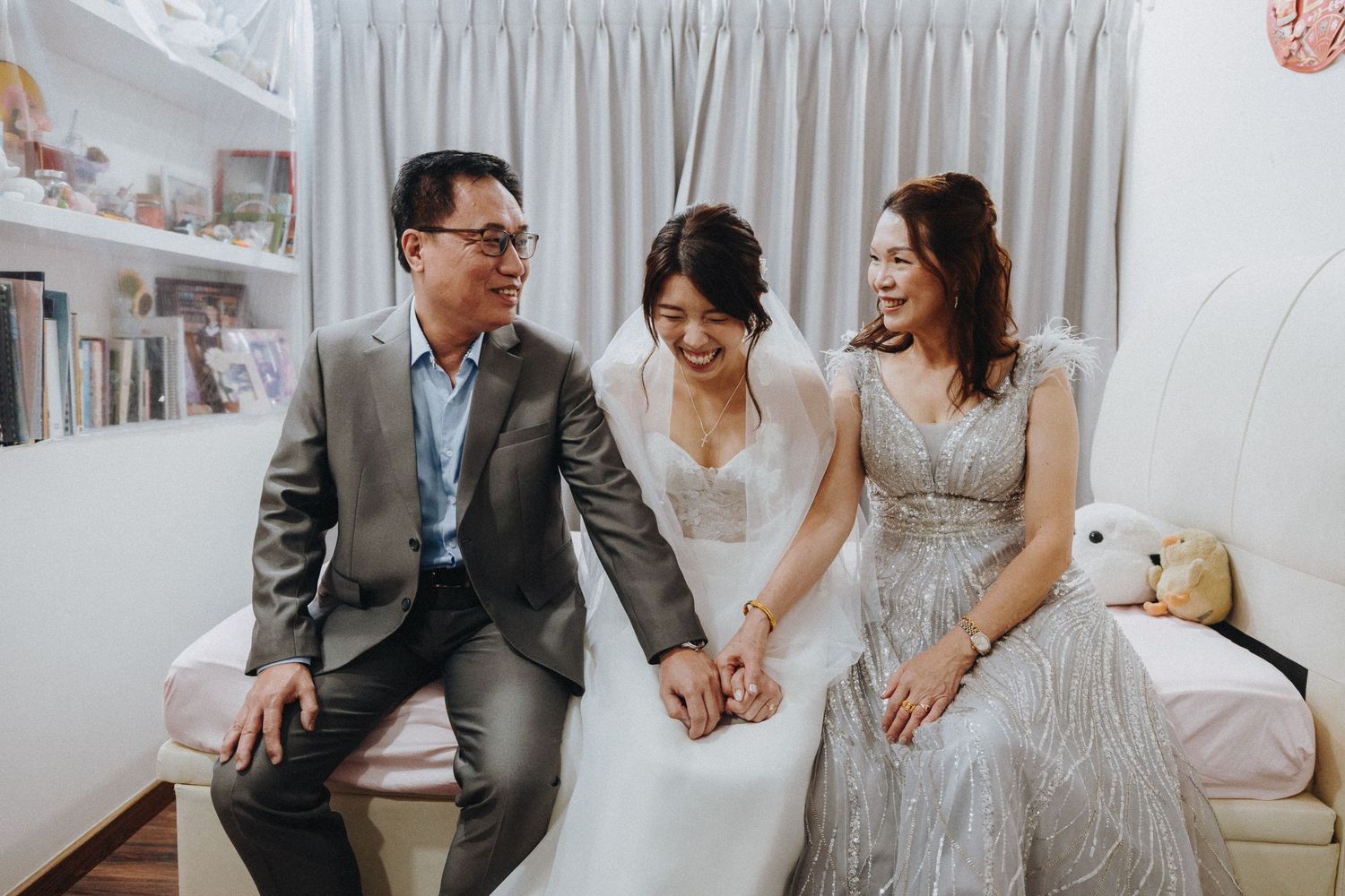 A modern couple laughs joyfully while seated together during their wedding celebration in a light-filled room.