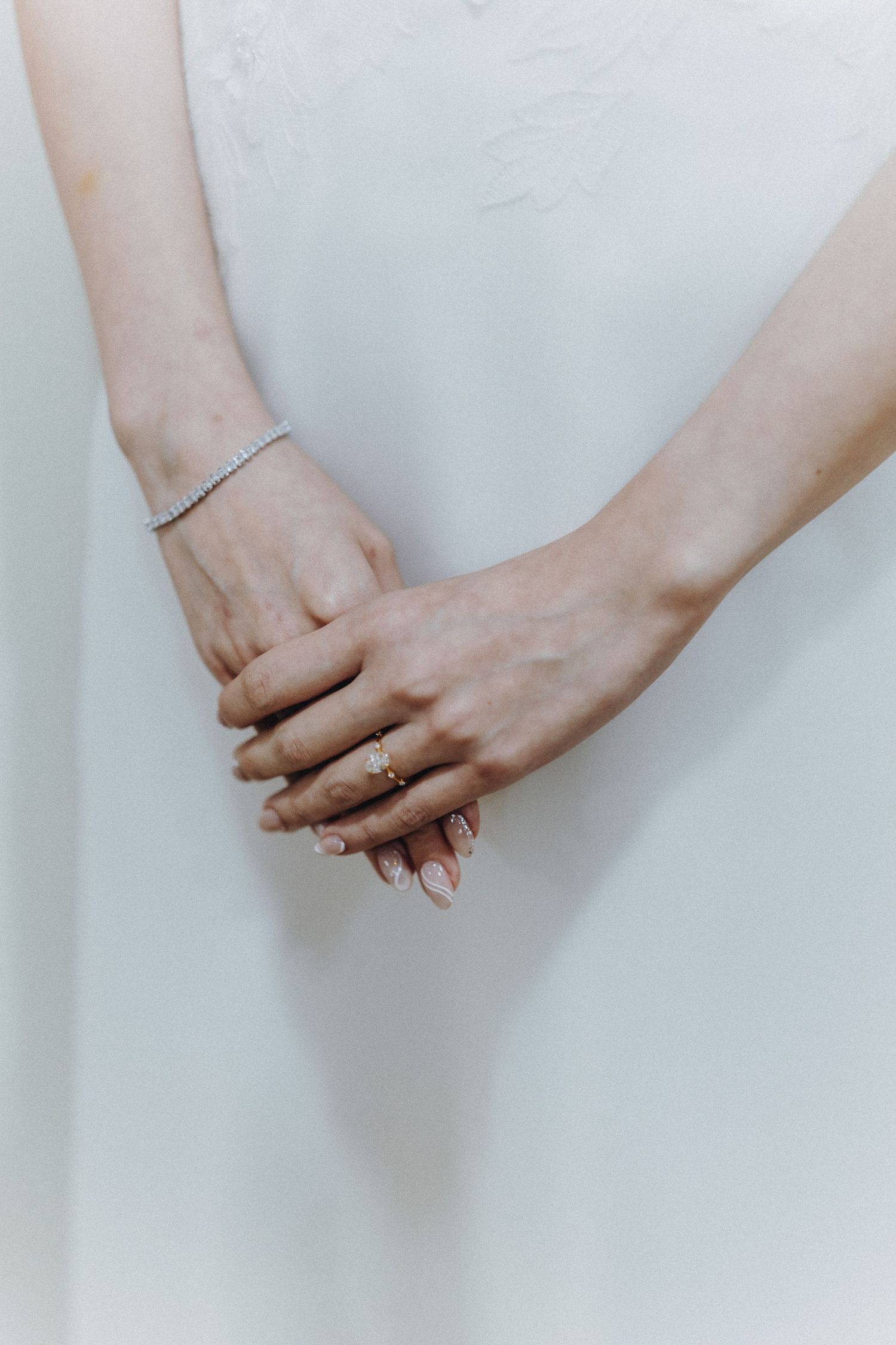 Close-up of hands with delicate jewelry against a white wedding dress background.