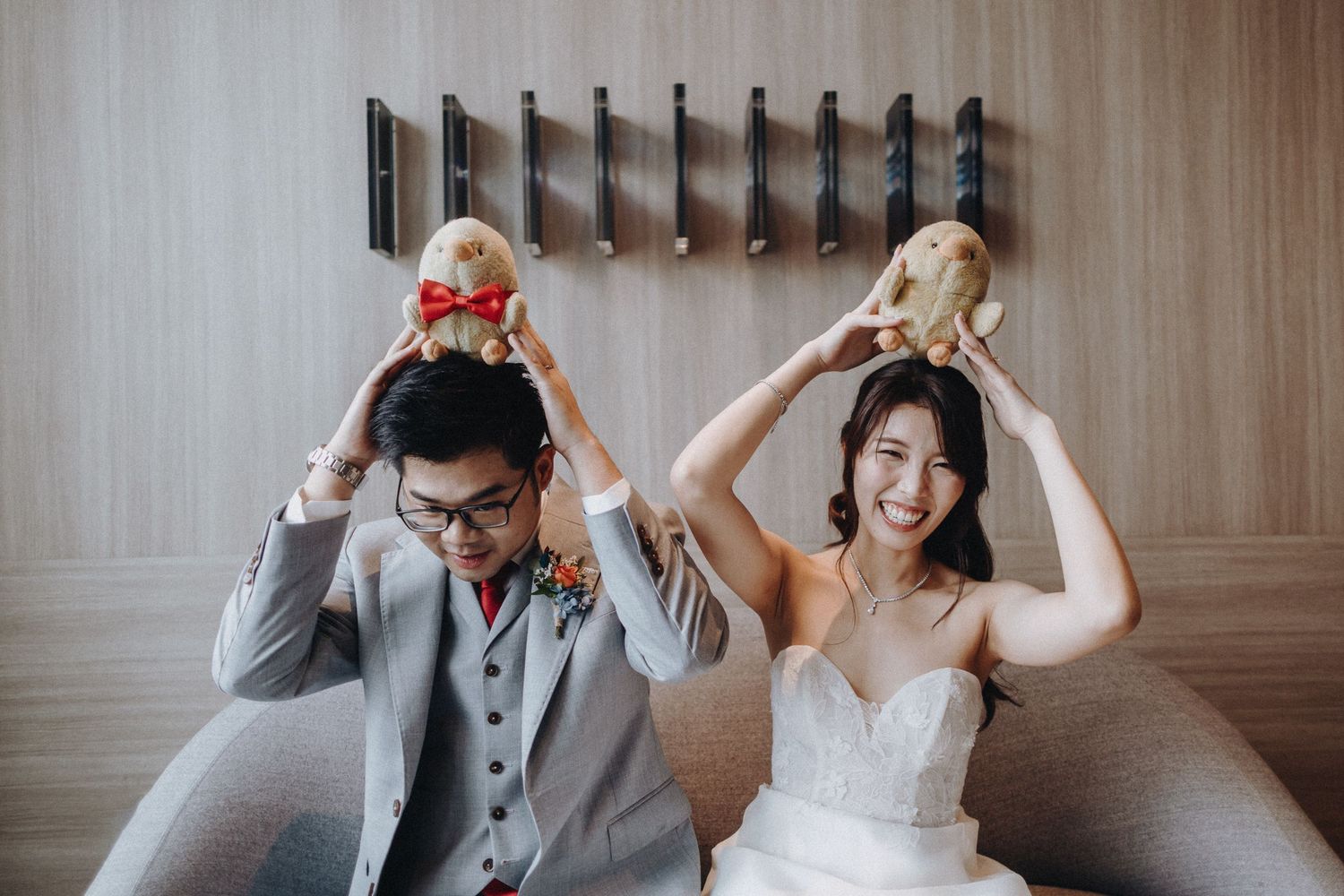 A playful wedding couple poses together against a wooden wall backdrop, showing joyful and silly expressions.