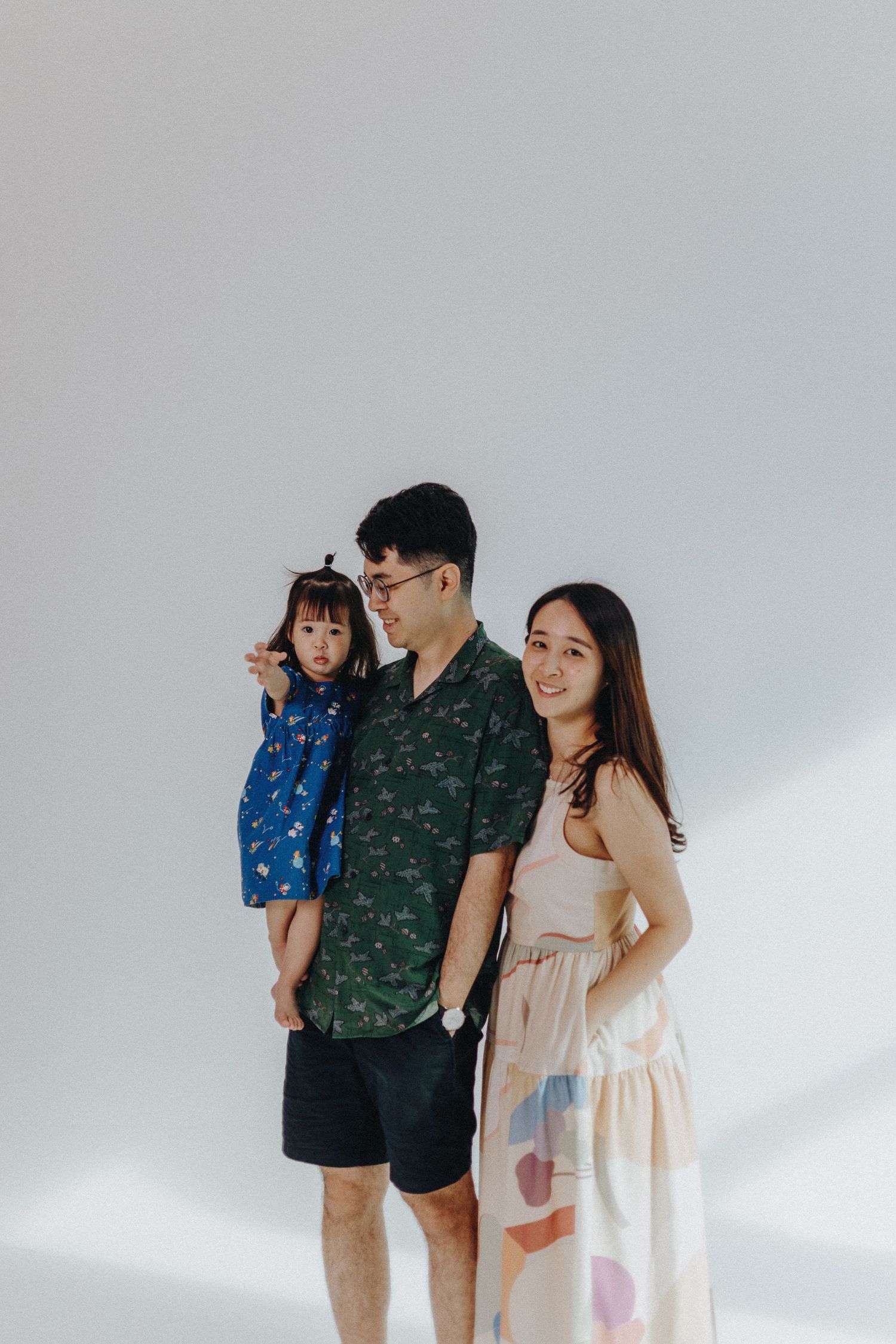 Family in coordinated outfits poses together against white backdrop in minimalist studio setting.