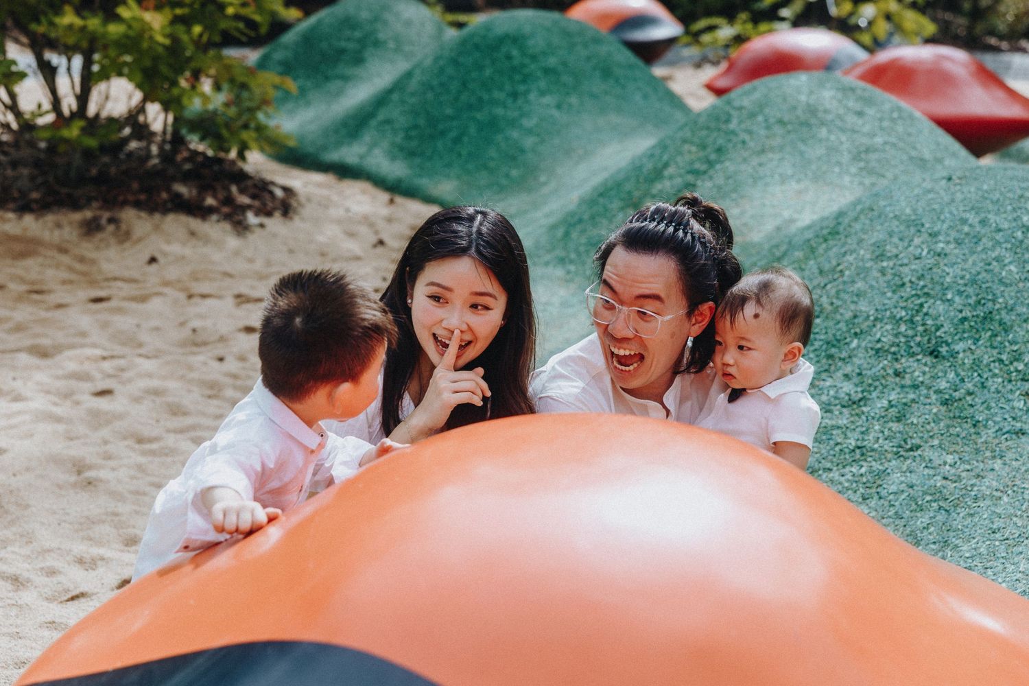 Family having fun and laughing together at a playground with colorful equipment.