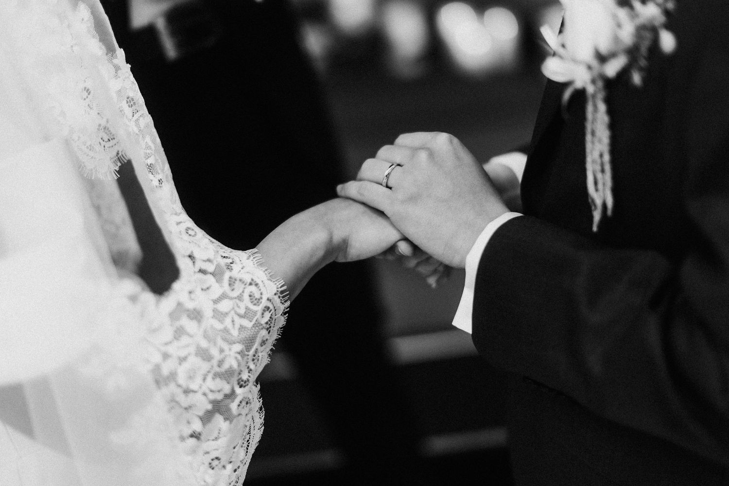 Close-up black and white photo of wedding rings and lace dress details.