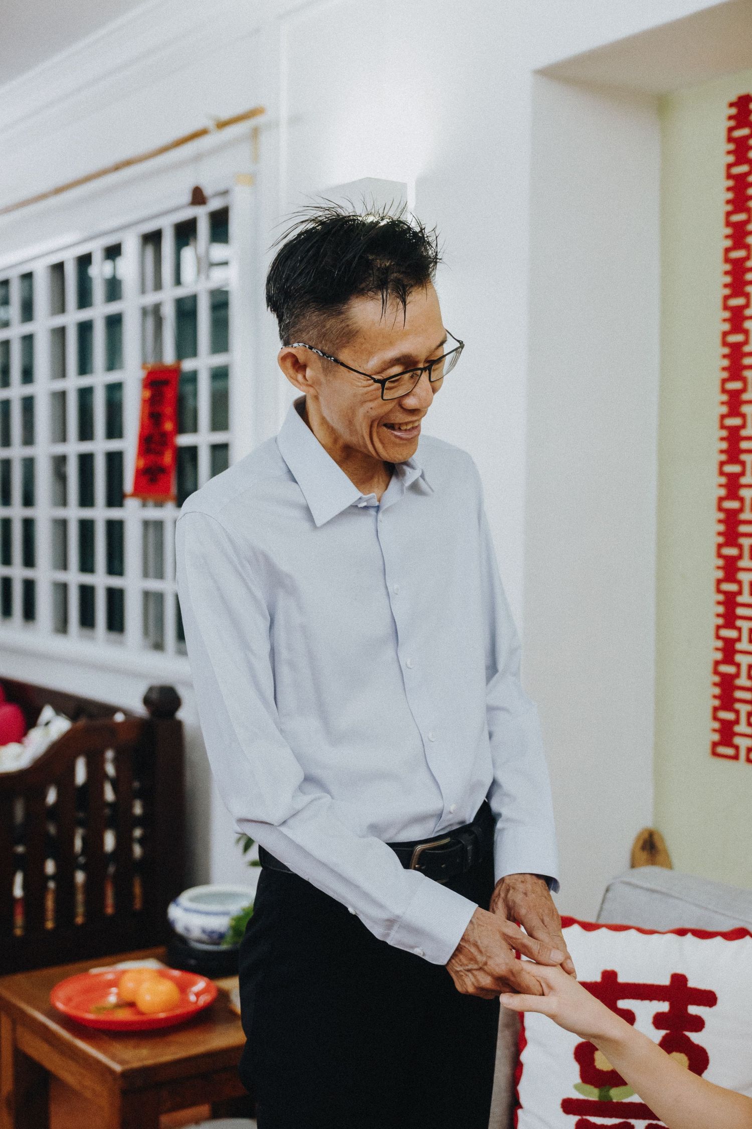 A person wearing glasses and a light blue dress shirt smiles joyfully during a celebration.