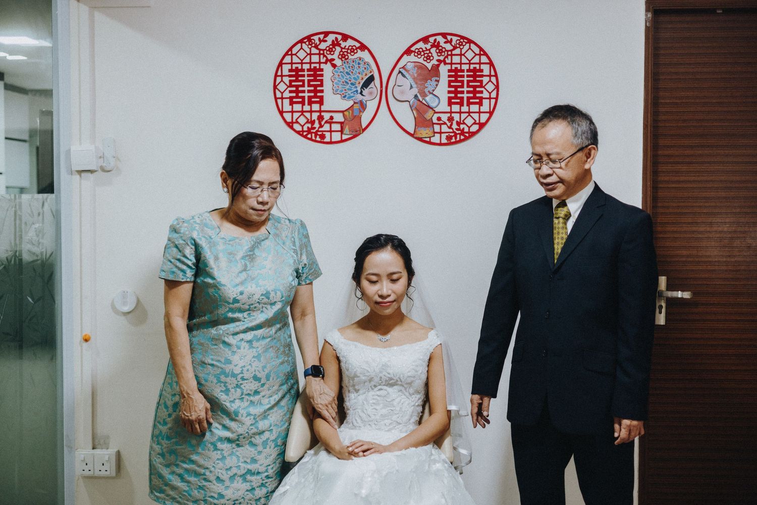 Three people in formal attire pose together in front of a wall with traditional Chinese paper-cut decorations.