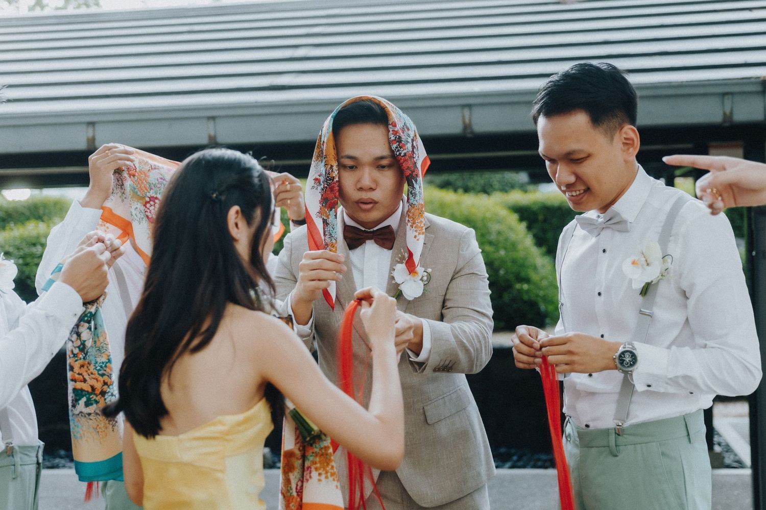 Group of wedding guests in formal attire interacting during an outdoor celebration.