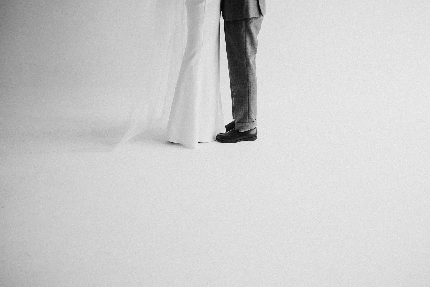 Black and white minimalist wedding photo showing just the bottom half of a bride and groom standing together.