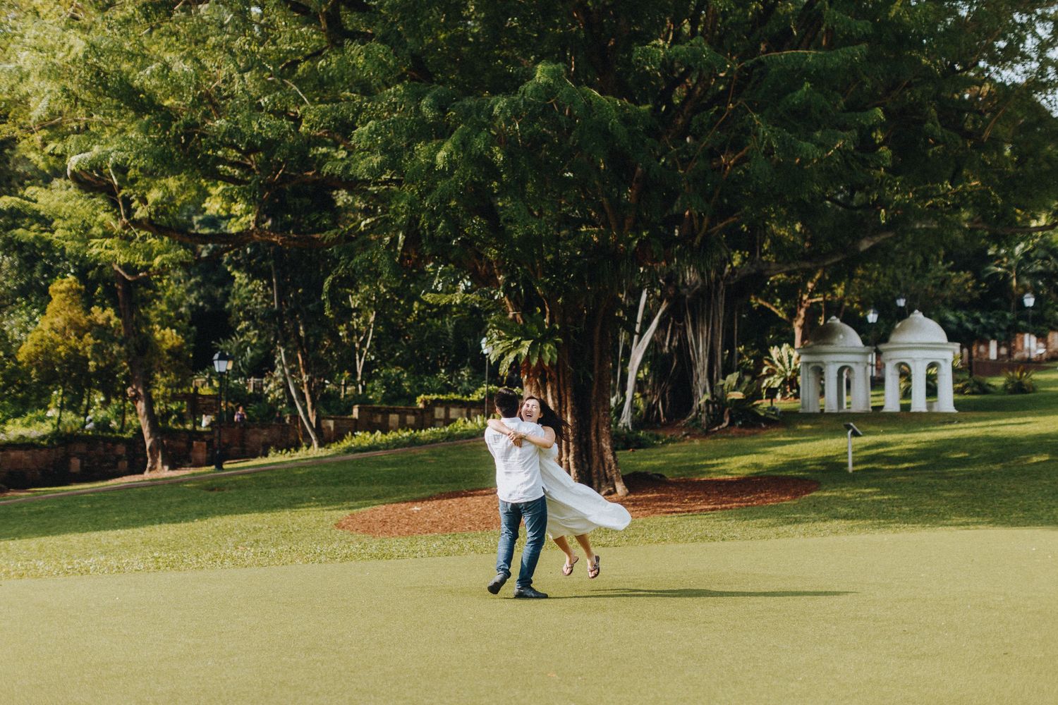 A romantic couple spins together on a manicured lawn with a white gazebo in the background.