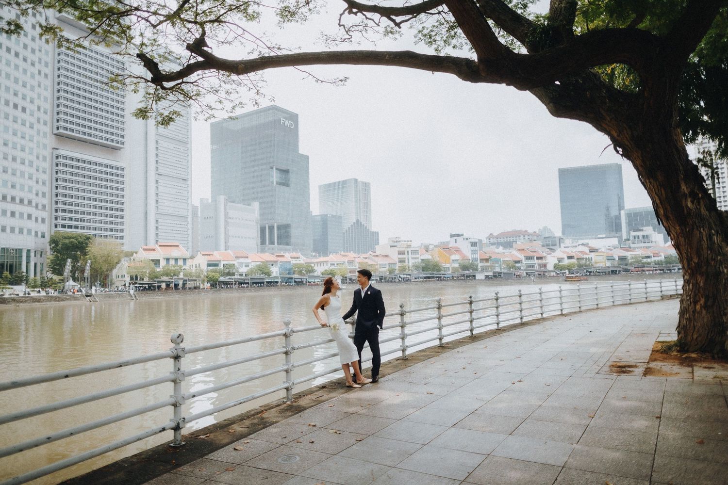 Misty waterfront promenade along Singapore's skyline with trees and modern skyscrapers in the background.