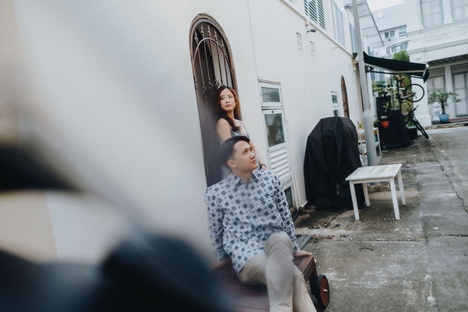 Person posing candidly against a white wall in an urban alleyway setting.