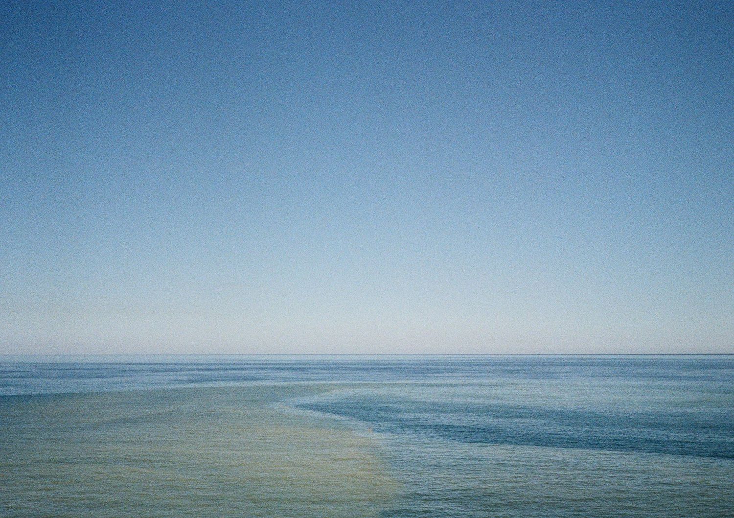 Panoramic view of a calm ocean horizon against a bright blue sky.