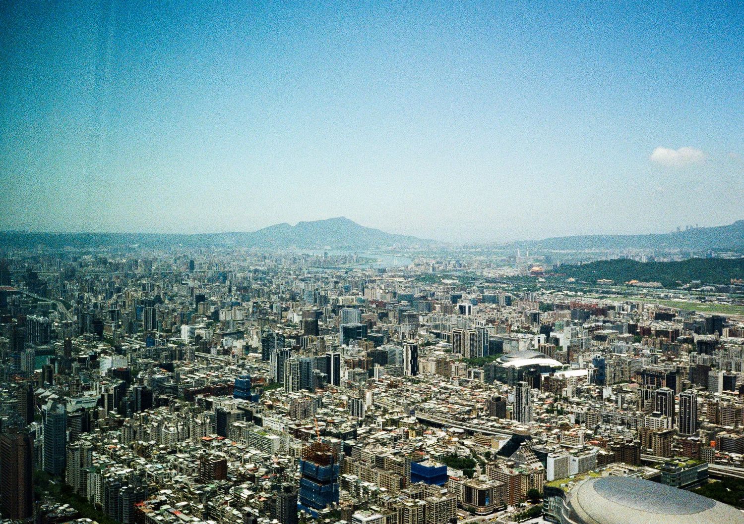 Panoramic cityscape view of a large urban area with mountains visible in the distance.