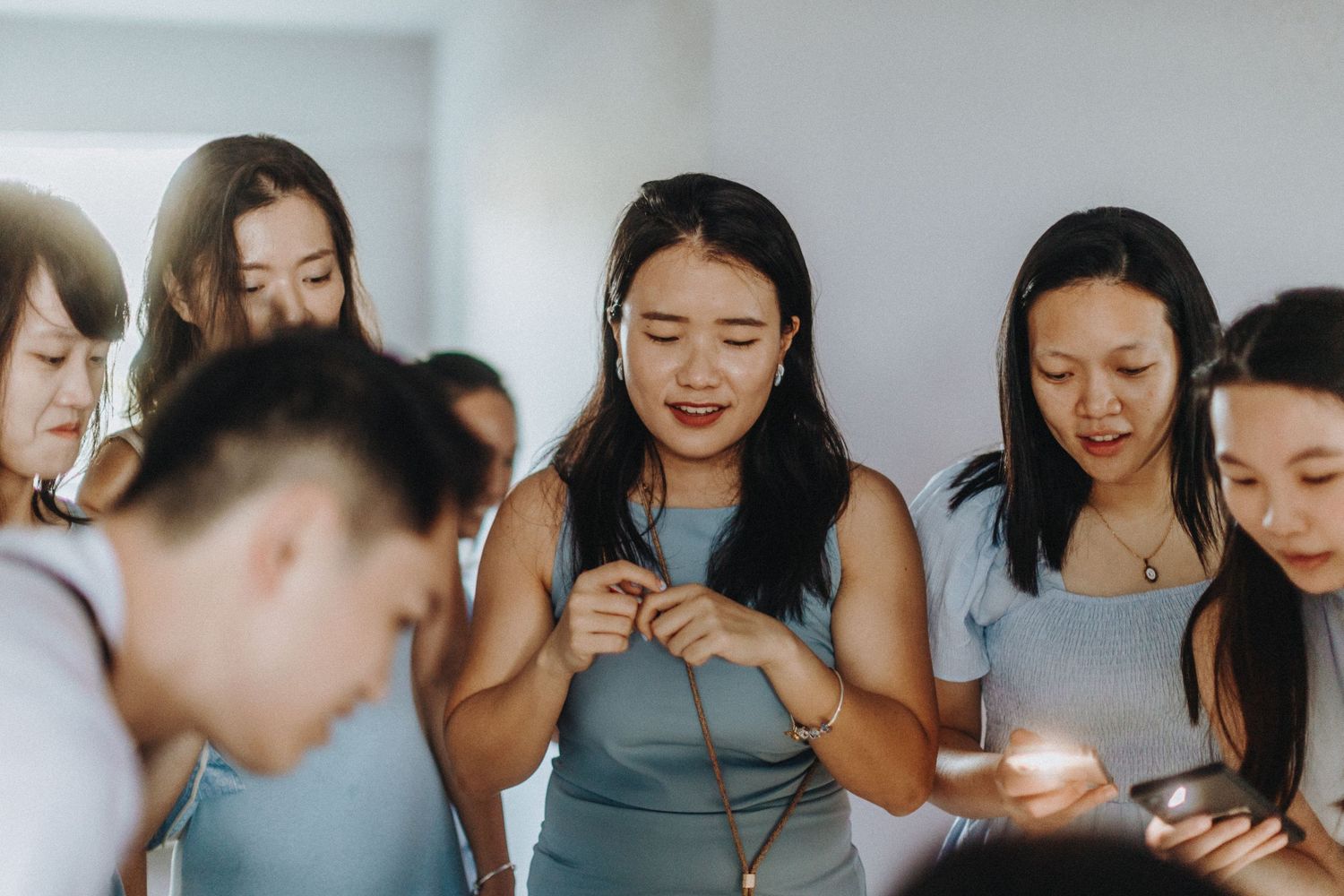 A group of people gather closely together while looking down at their mobile phones in a bright indoor setting.