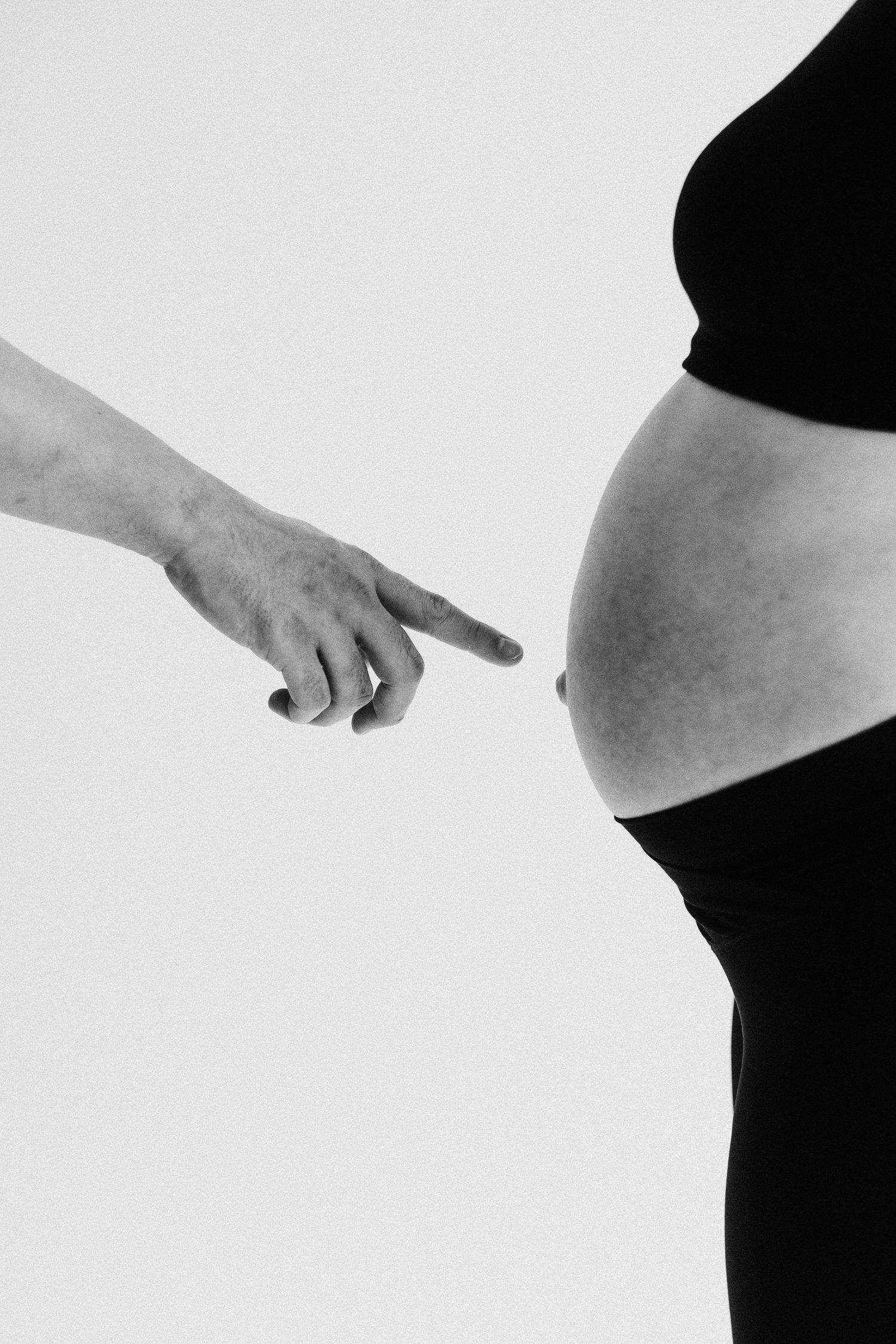A black and white image shows a hand pointing at a pregnant belly in silhouette.