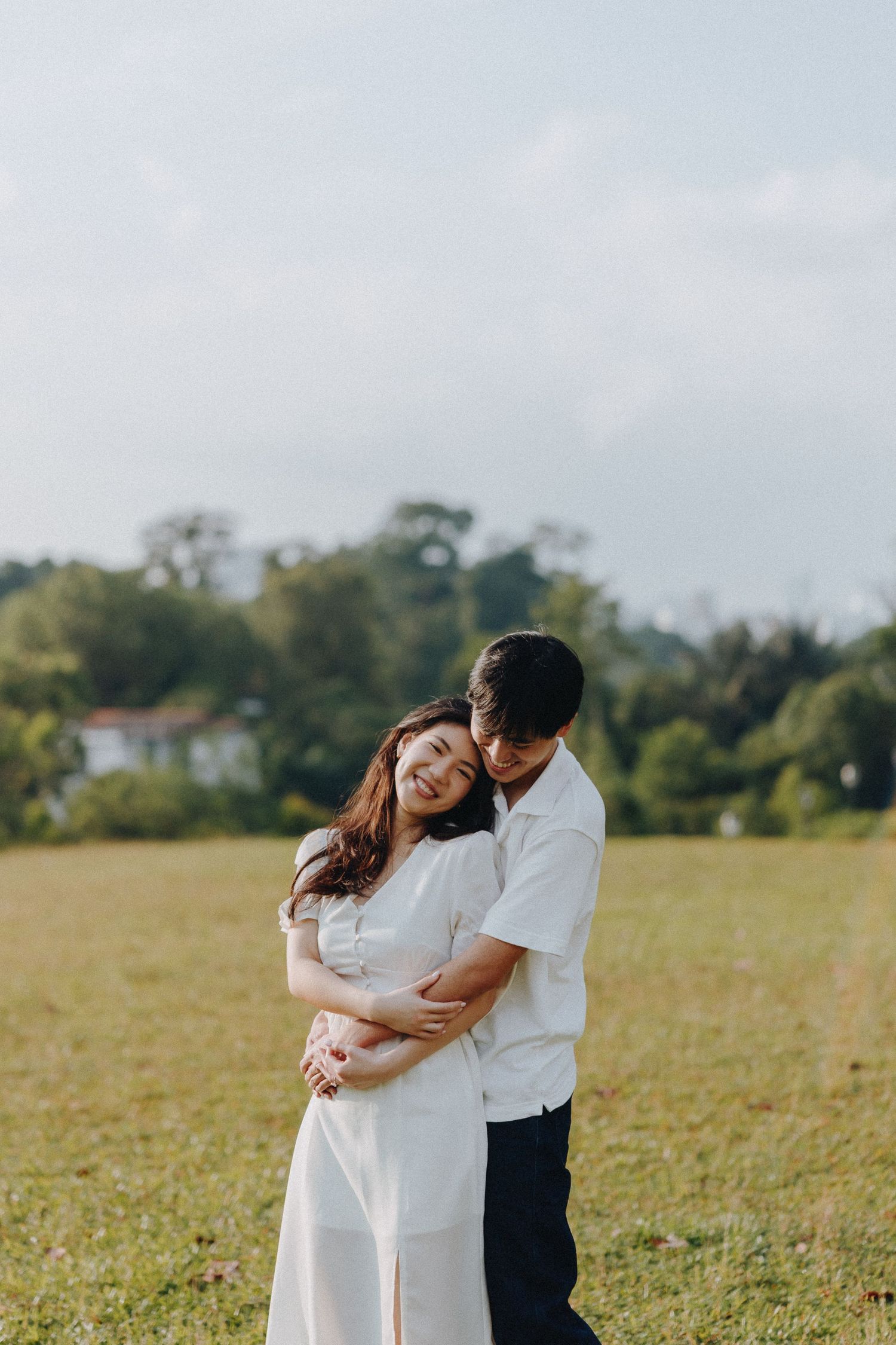 A romantic embrace between a couple wearing white and navy in a sunny meadow.
