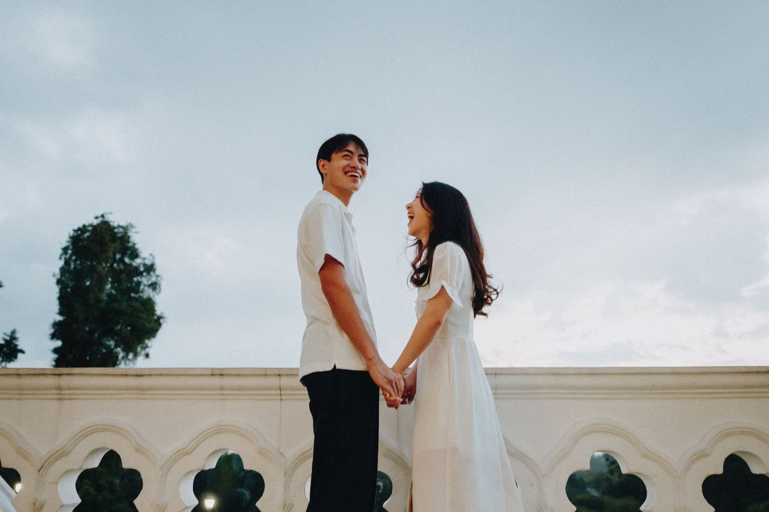 A couple shares a tender moment in front of a white wall during an outdoor wedding photo session.