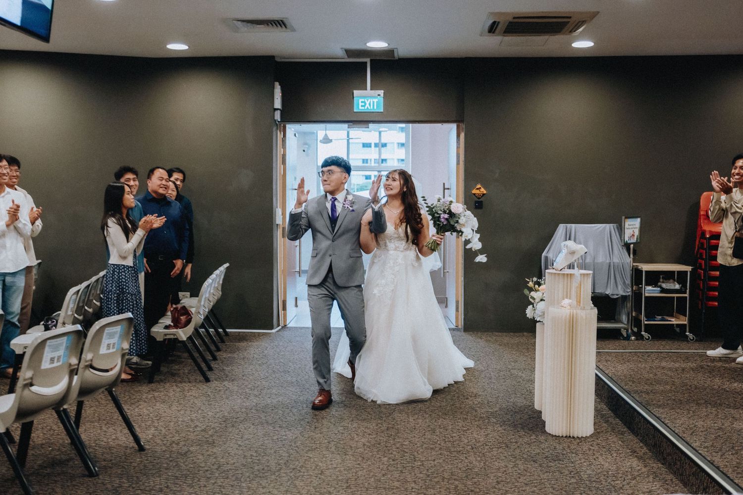 Wedding guests and a bride in white gather in a modern indoor venue with dark walls and recessed lighting.