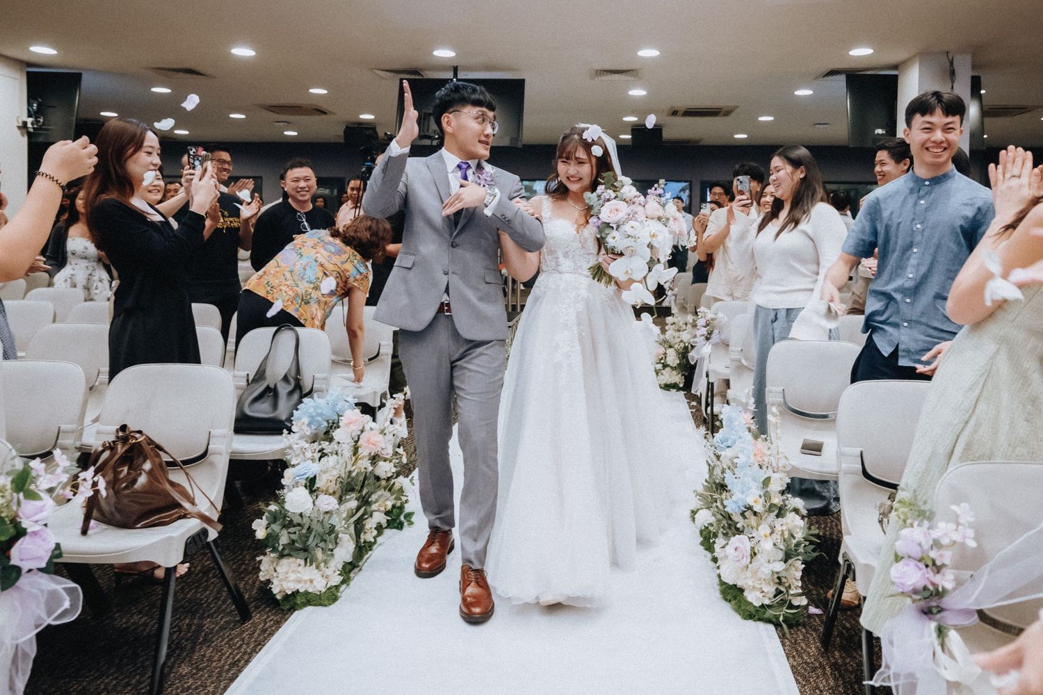 Wedding guests in white attire gather around tables decorated with floral centerpieces at an elegant reception.