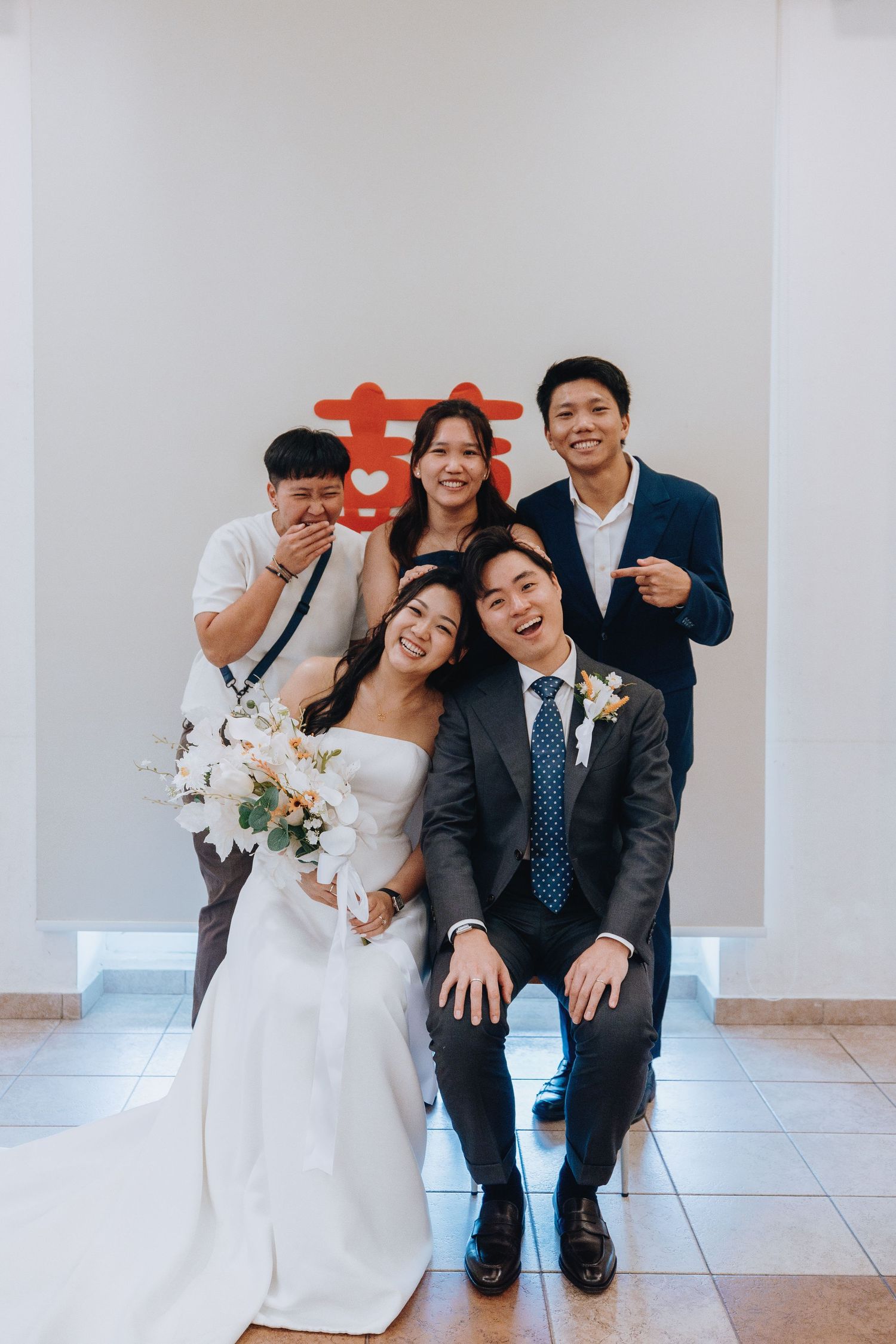 Bride and groom pose with wedding party in front of red double happiness symbol.