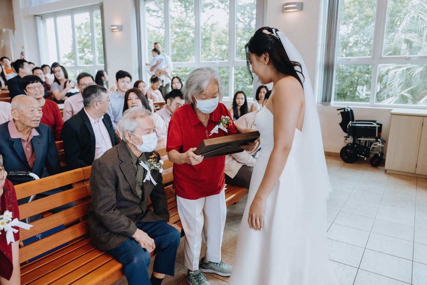 Bride presenting gift to elderly seated guests during wedding ceremony.