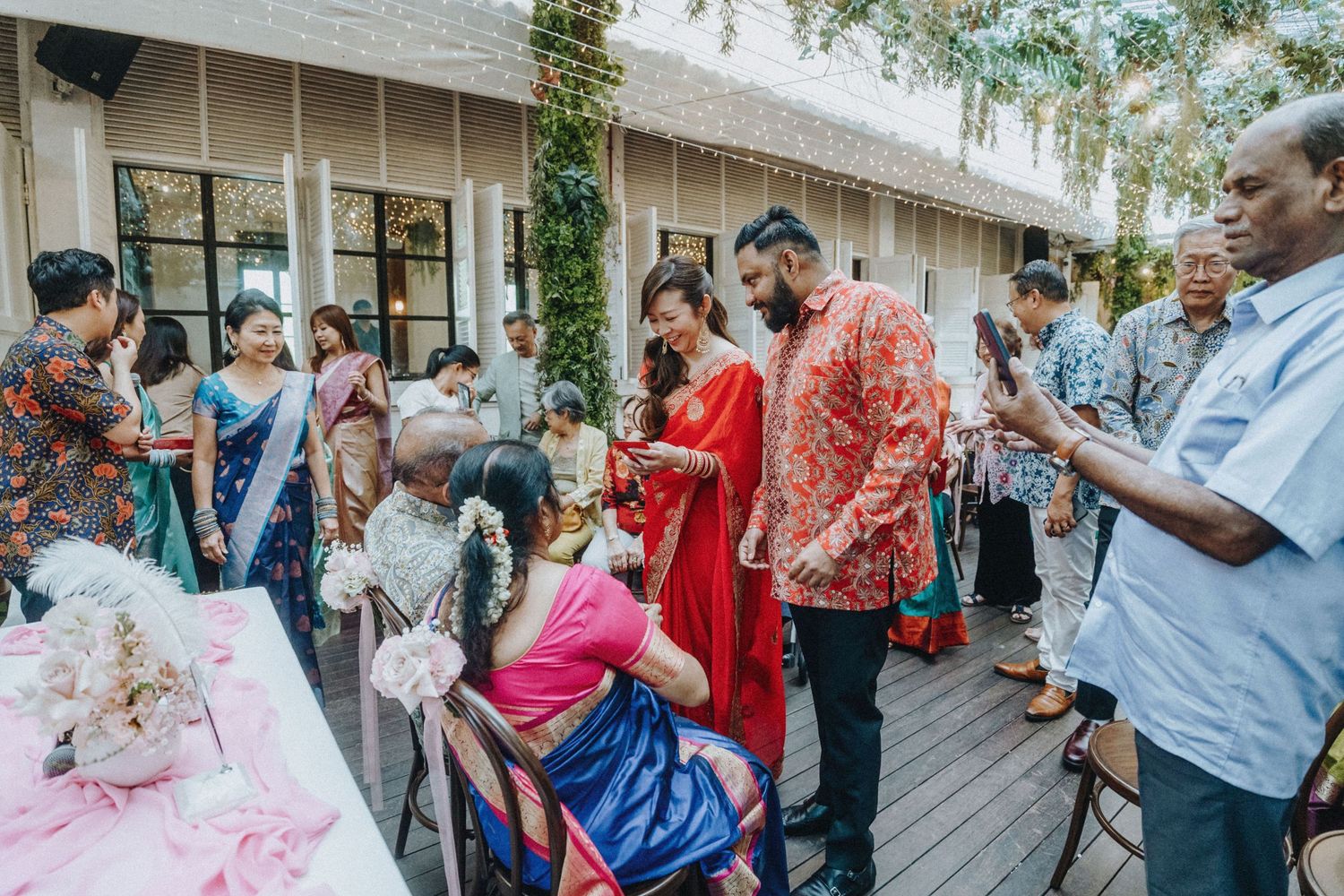 Guests in colorful traditional Indian attire celebrate at an outdoor wedding reception on a decorated patio.