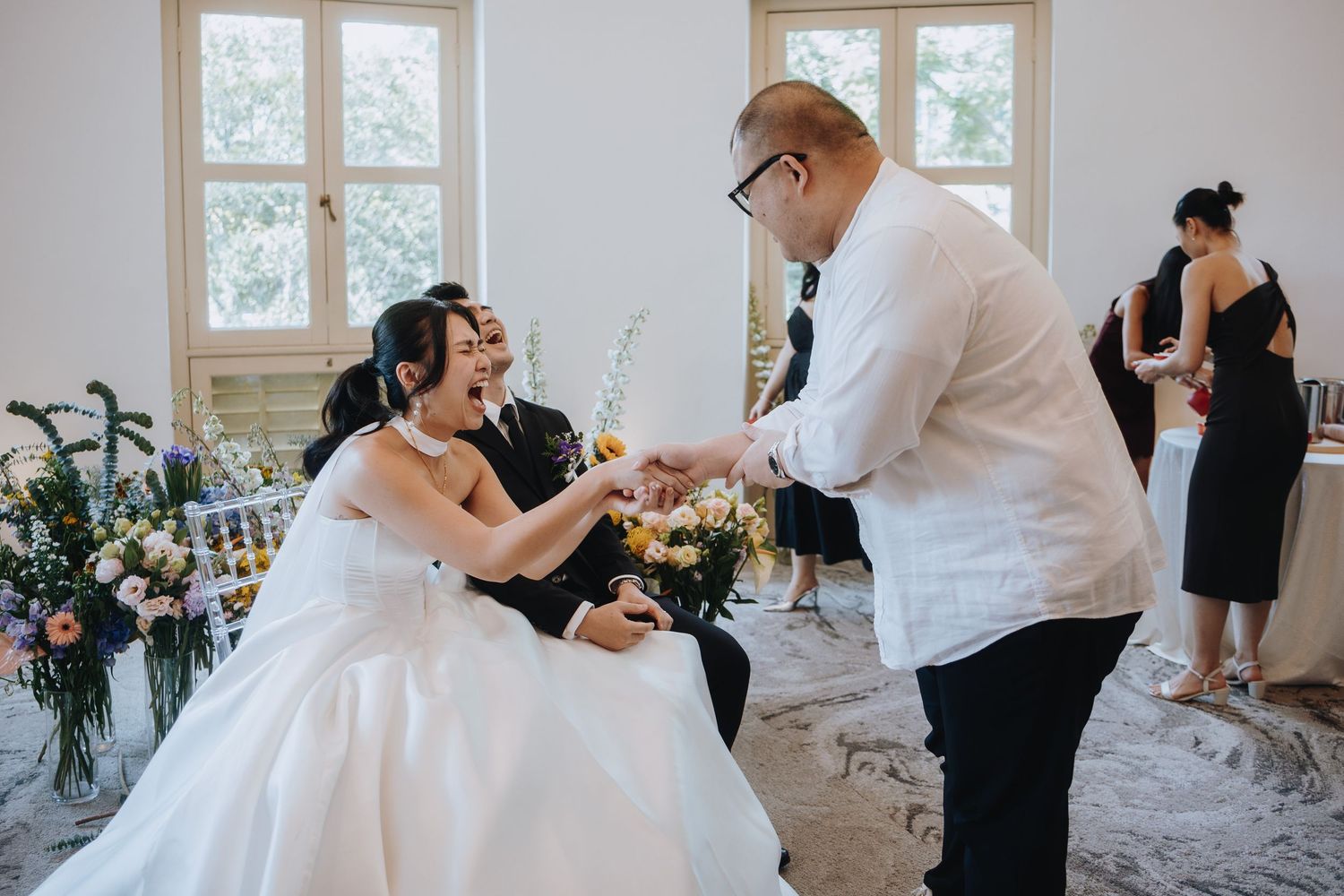 Bride laughs joyfully while receiving a gift from a guest at her wedding reception.