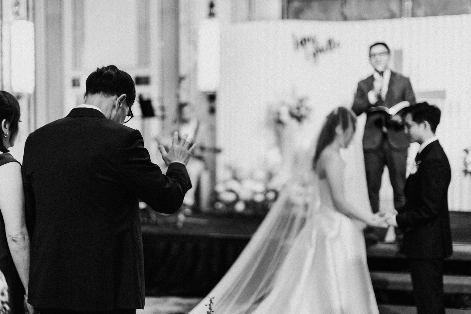Black and white photo of a wedding ceremony with guests clapping in a formal venue.
