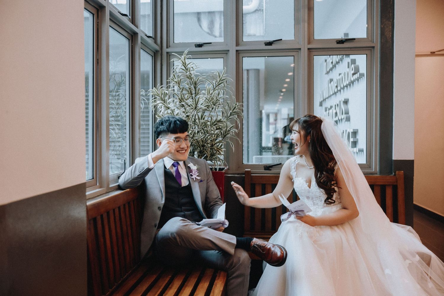 A couple shares a quiet moment on a wooden bench by large windows.