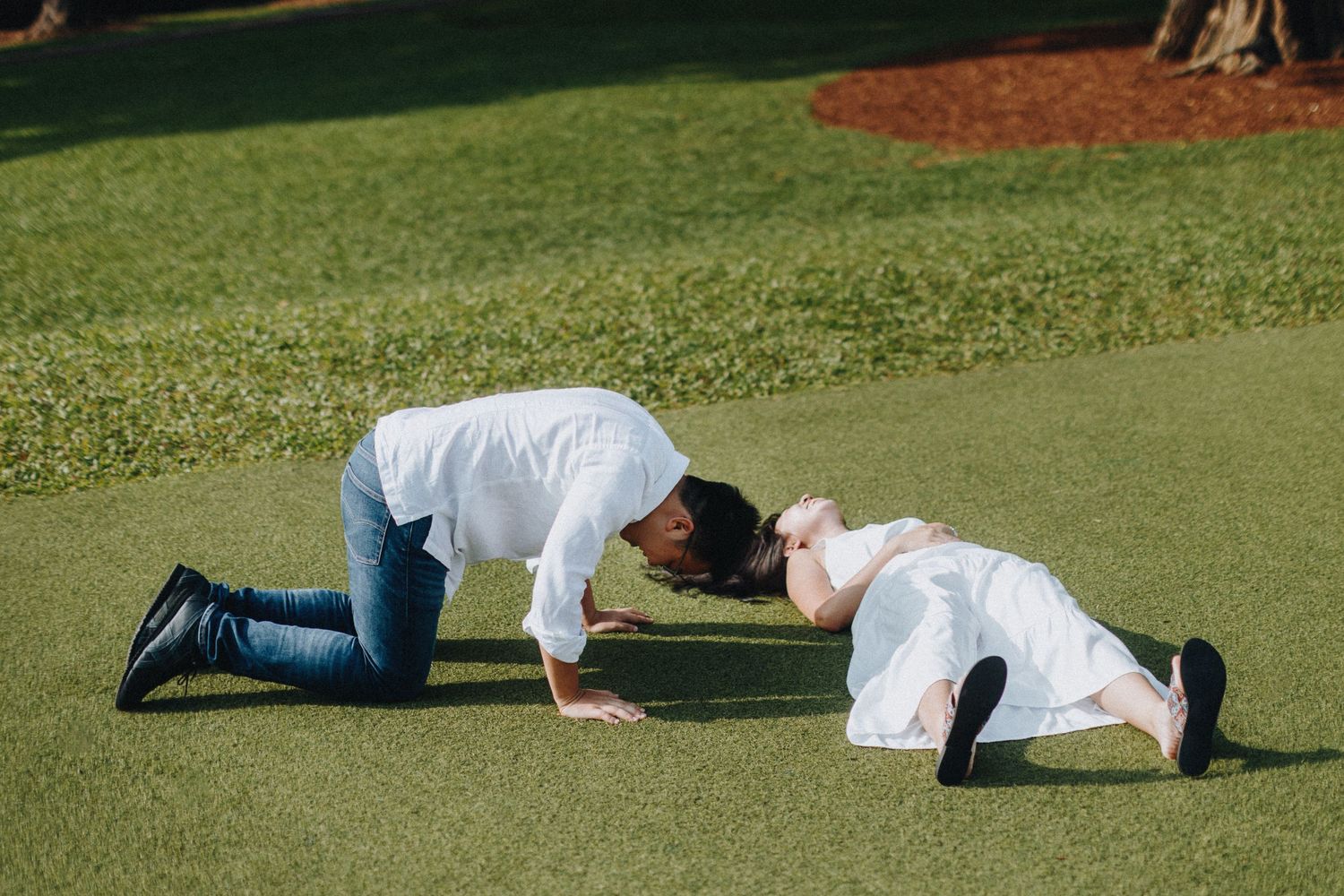 A couple lies playfully on a green lawn during an outdoor photoshoot.