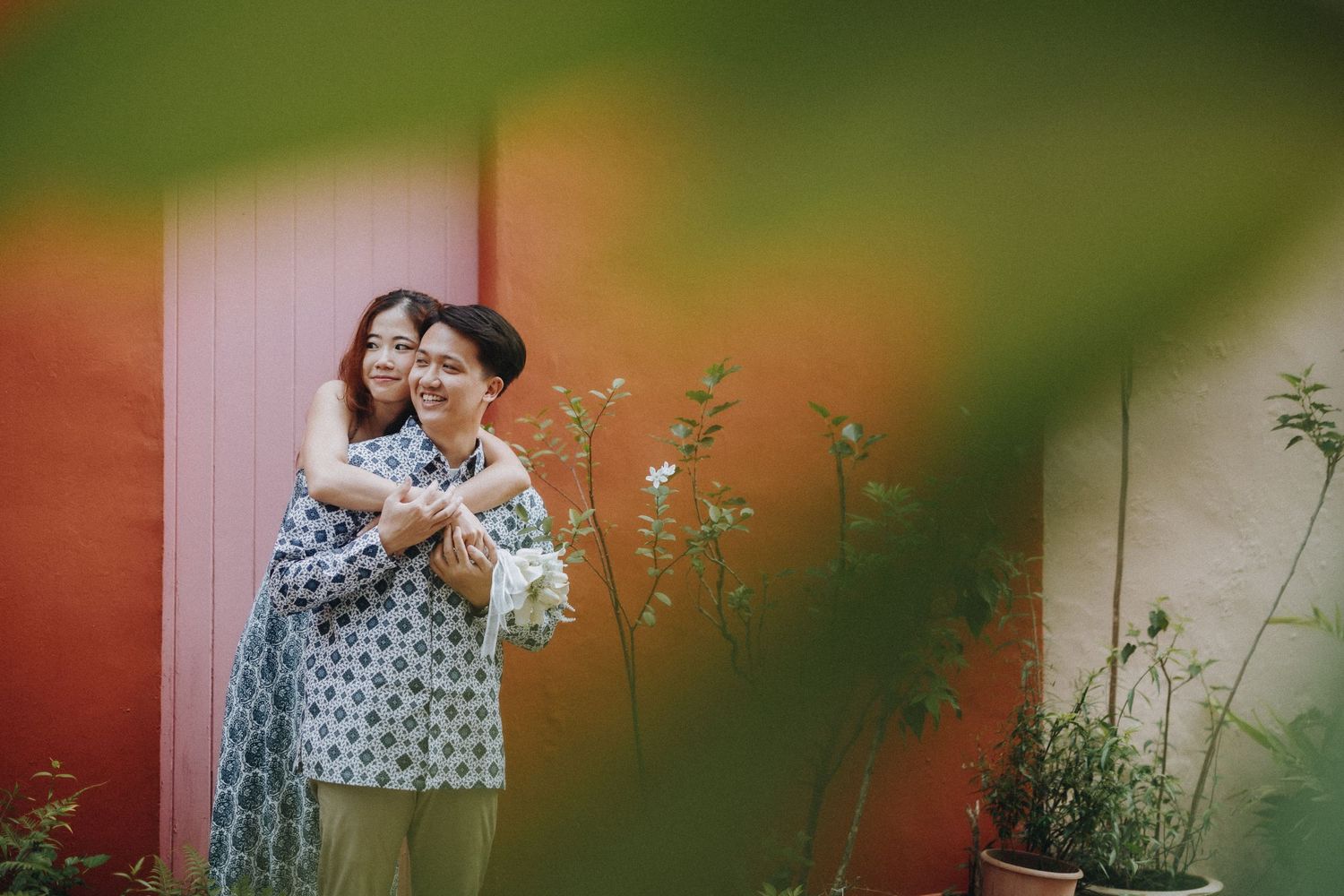 A romantic couple pose together in front of a blurred orange and green background.