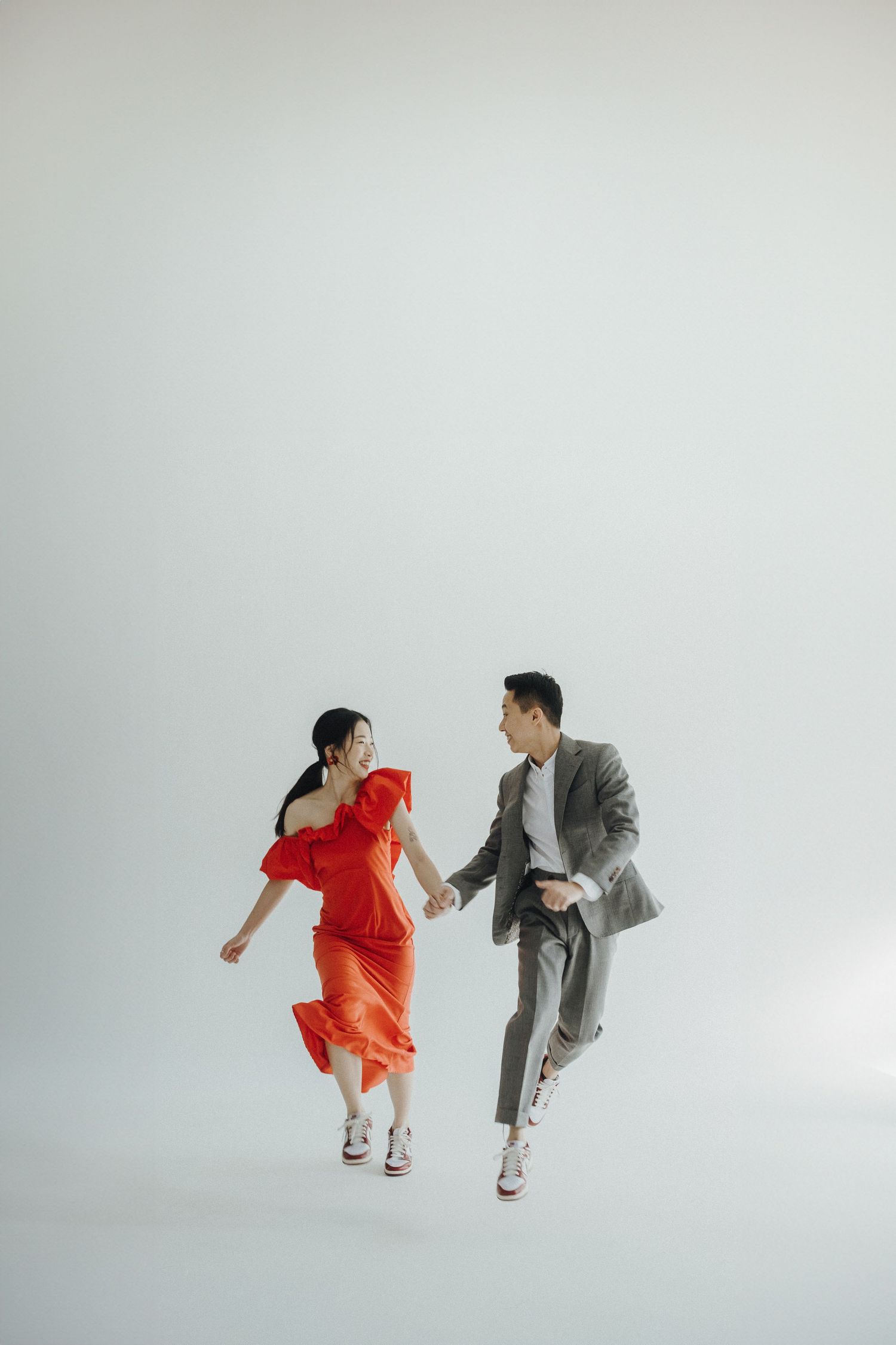 Two people in orange and gray outfits jumping and posing playfully in a minimalist studio setting against a white backdrop.
