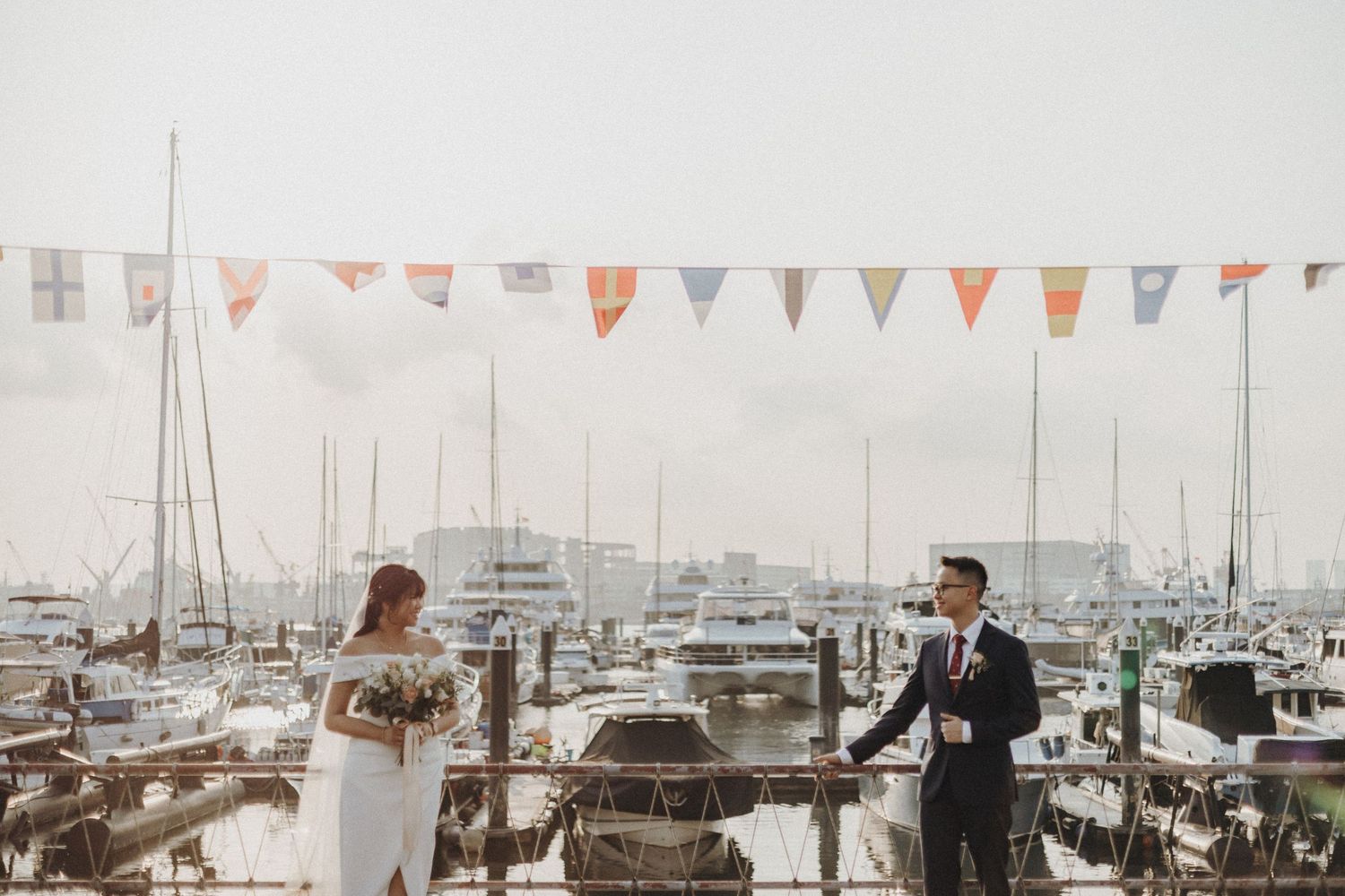 A marina wedding scene with colorful flags hanging above and boats docked in the background.