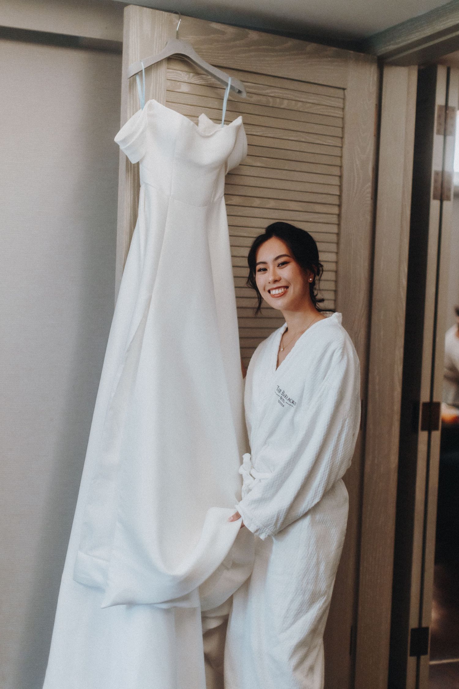 A classic white wedding gown with off-shoulder design hangs in a dressing room.