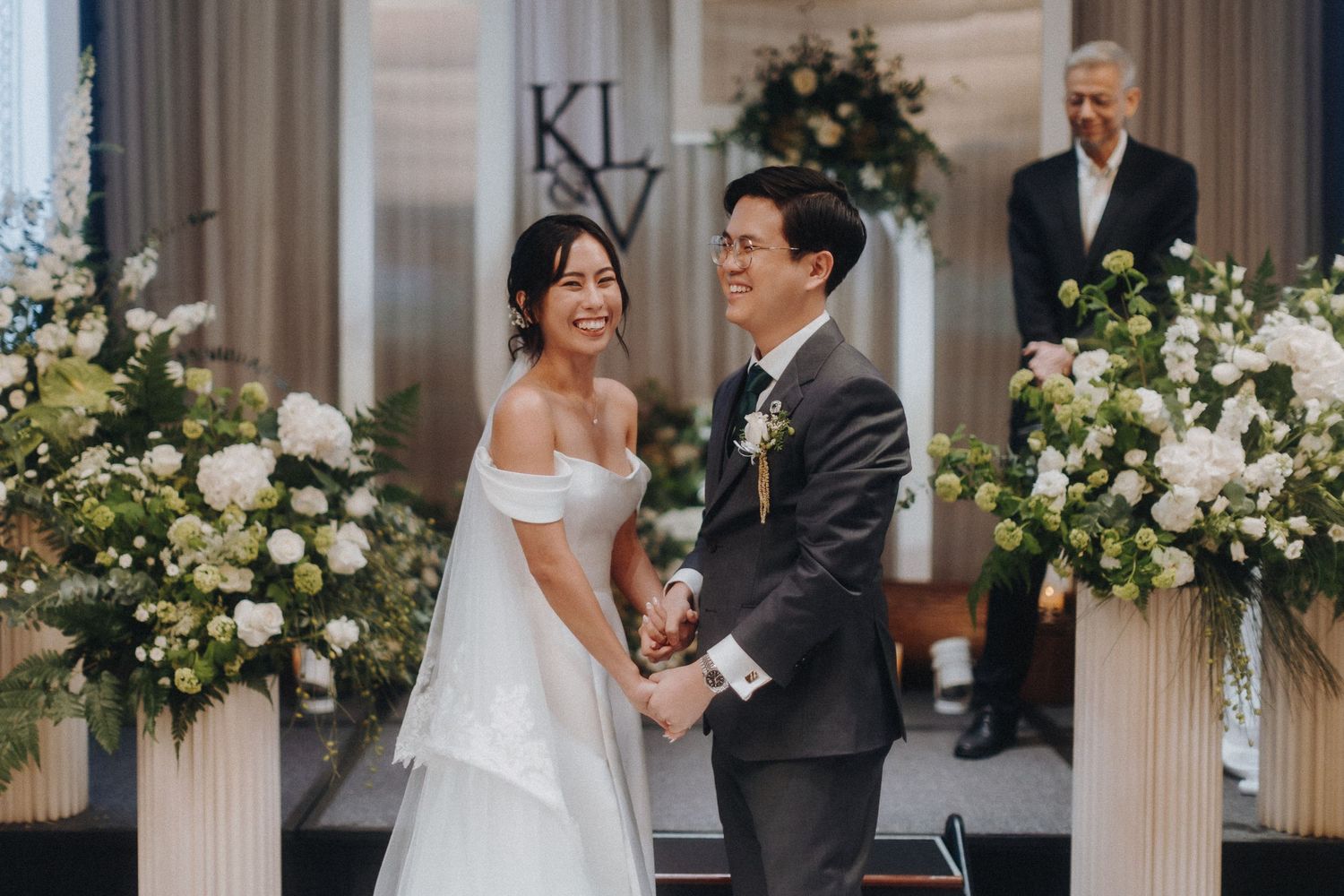 Elegant wedding ceremony setup with white floral arrangements and classical columns in an indoor venue.