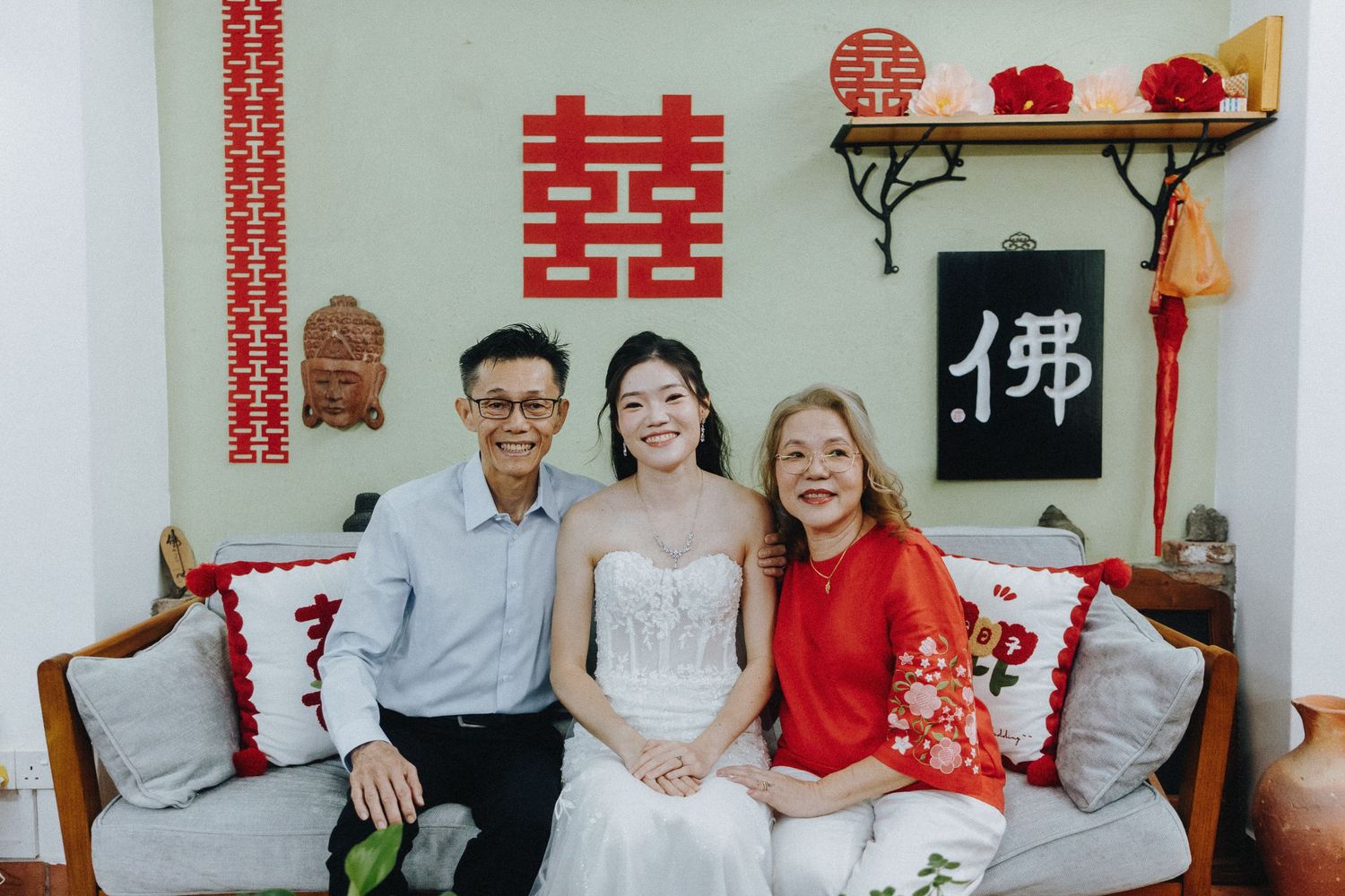 A family poses against white walls adorned with traditional Chinese decorations and red double happiness symbols.