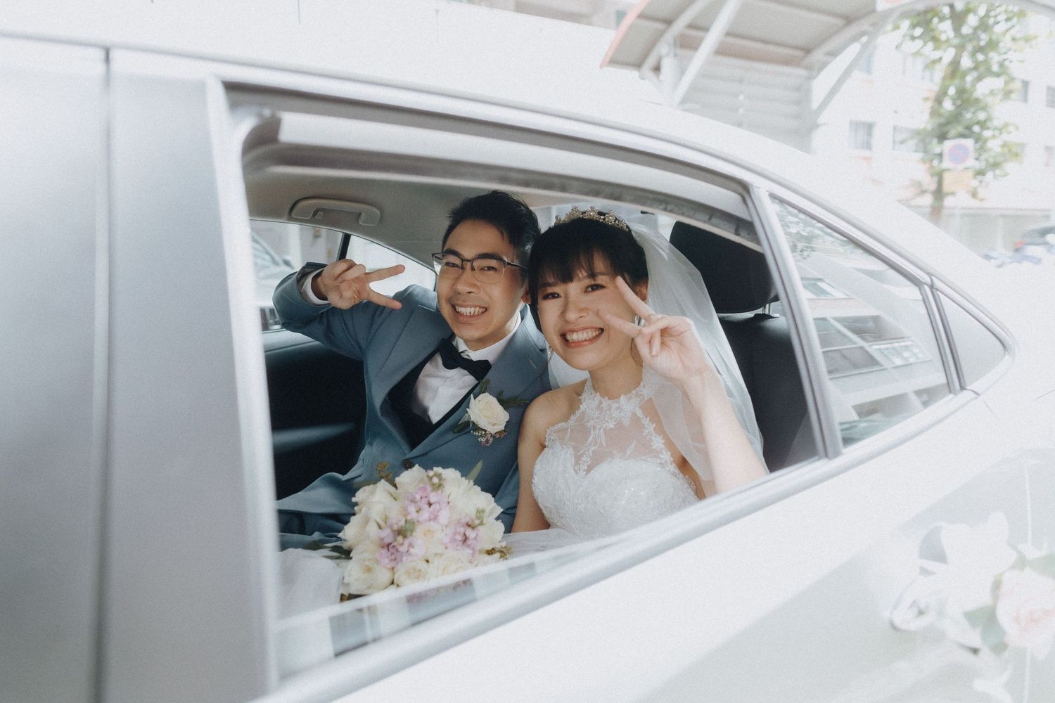 A joyful moment captured through a car window with formal attire and a pink bouquet.