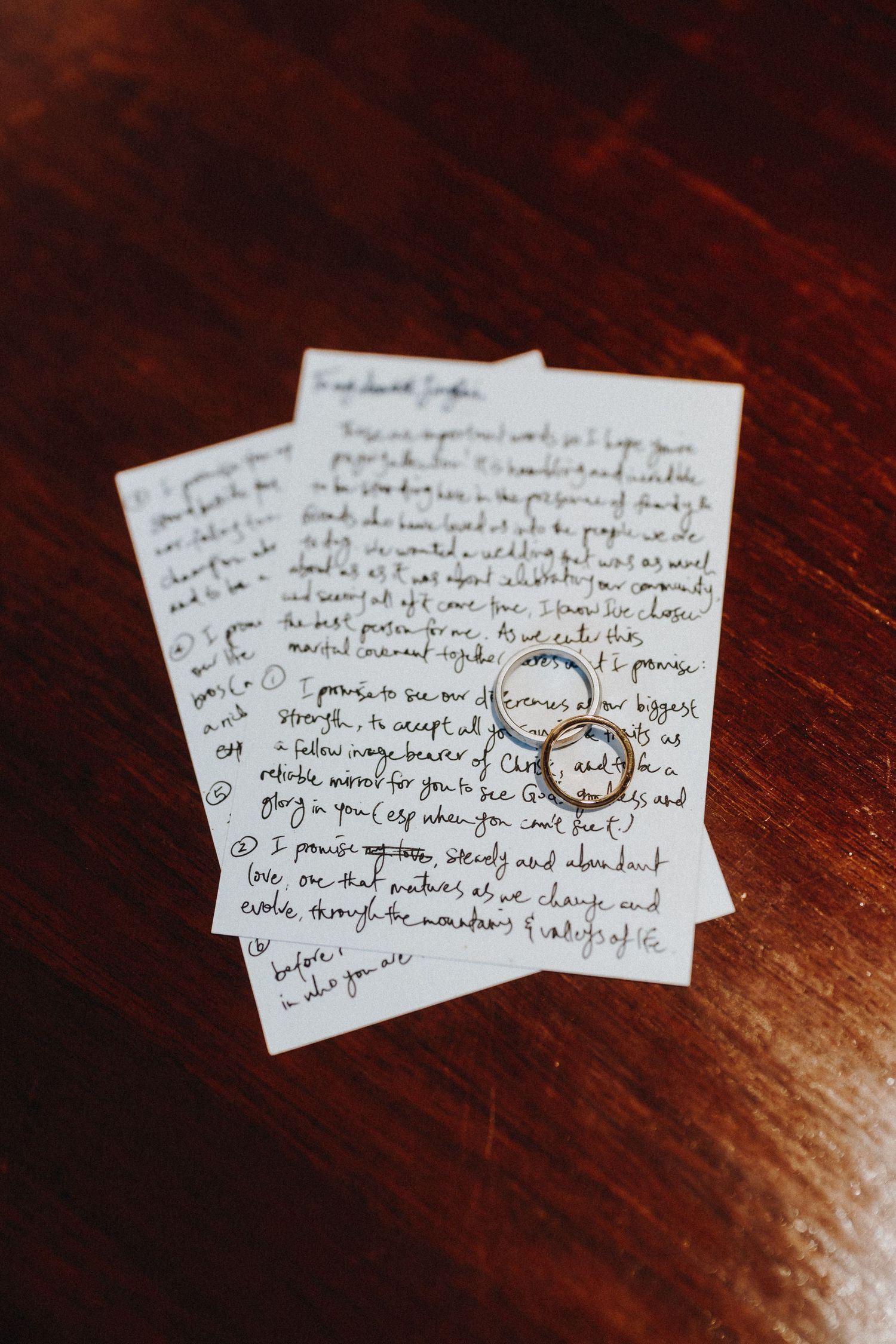 Wedding rings resting on handwritten love letters on a dark wooden surface.