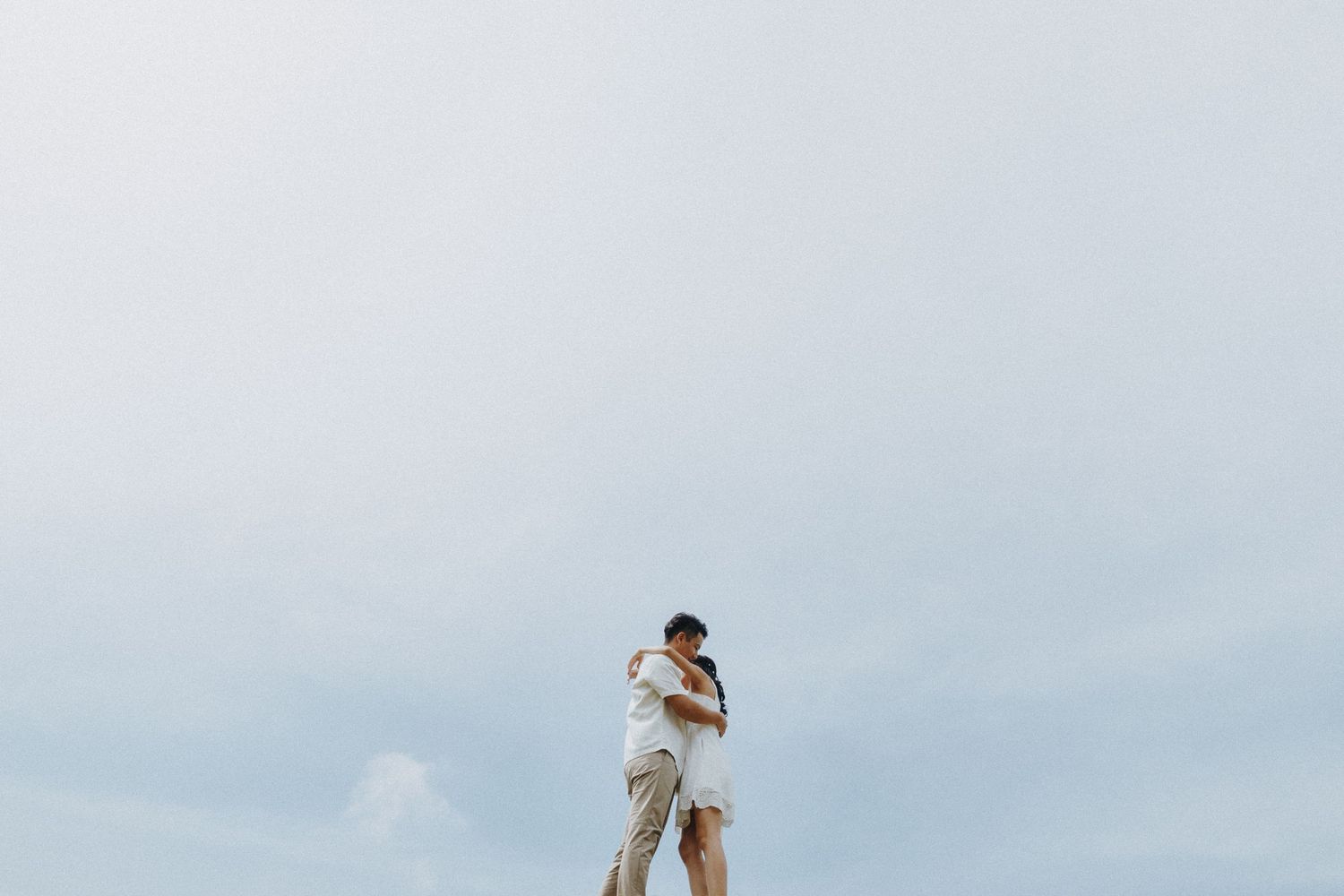 Couple in white outfits dancing playfully in a grassy outdoor setting during a lighthearted photoshoot.