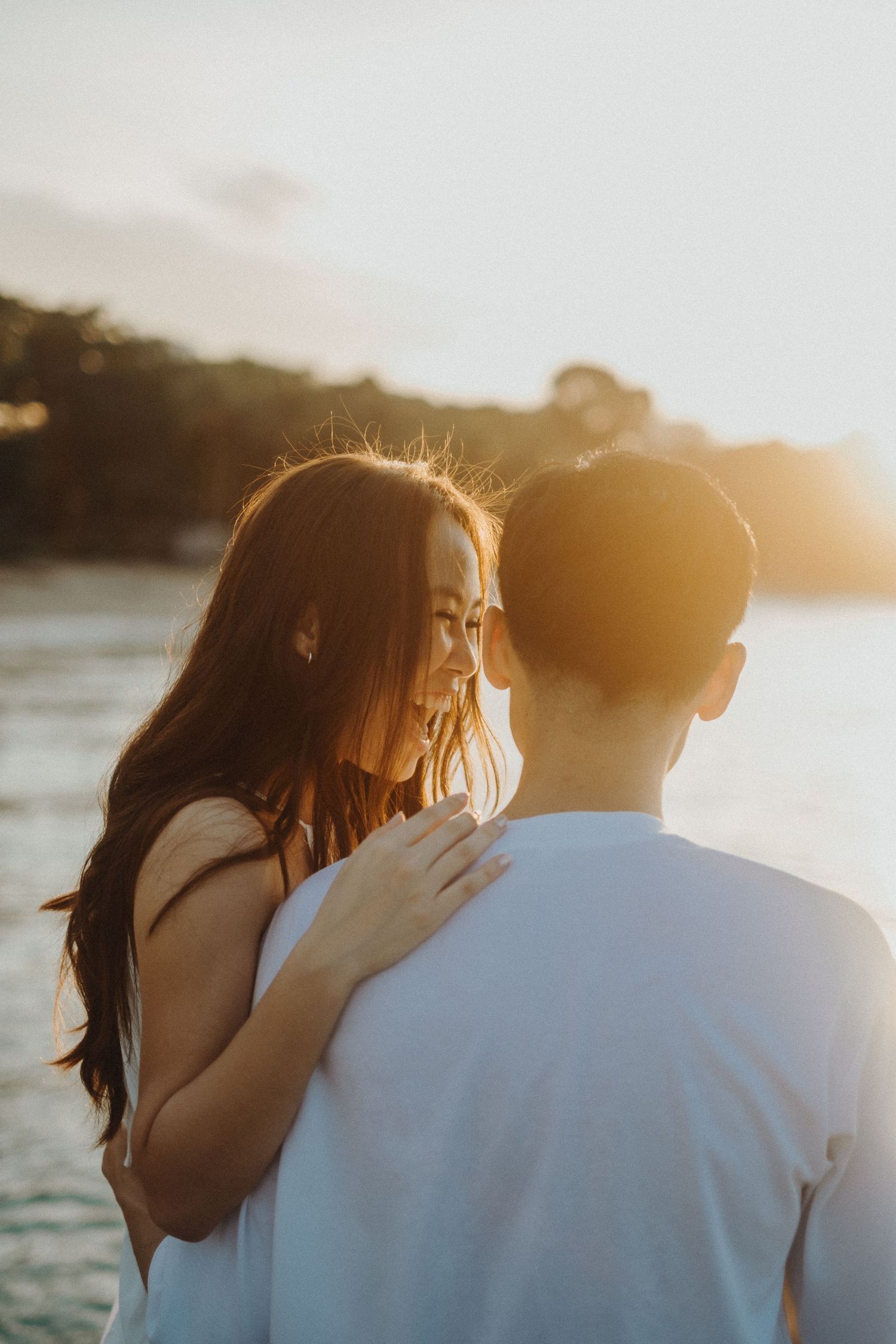 Intimate couple sharing a tender moment against golden sunset light by the ocean.