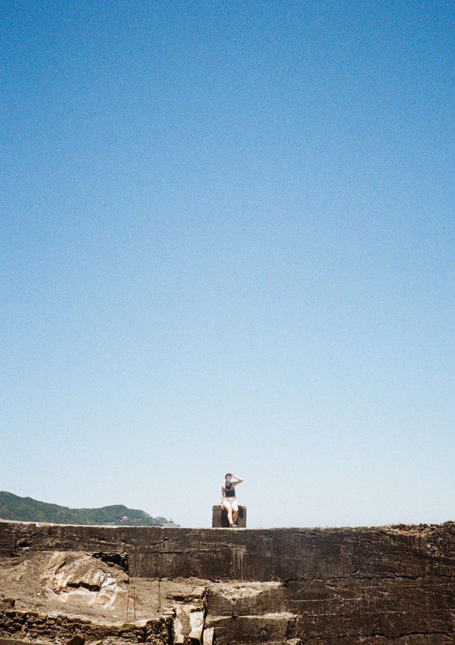 Isolated figure stands atop a stone wall against clear blue sky in arid landscape.