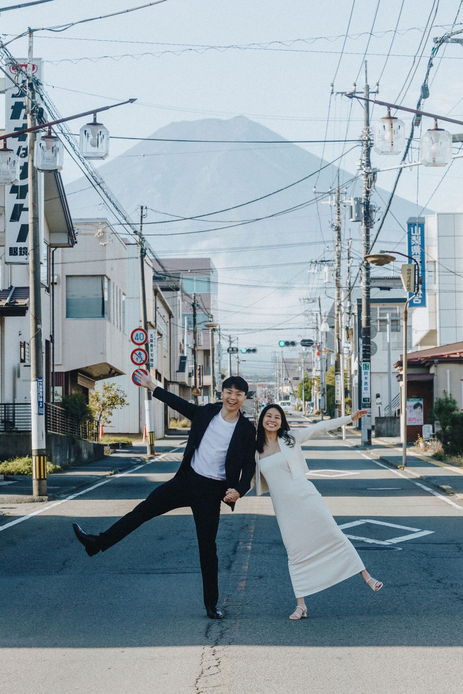 Playful couple dancing in the middle of an empty Japanese street with mountains in background.