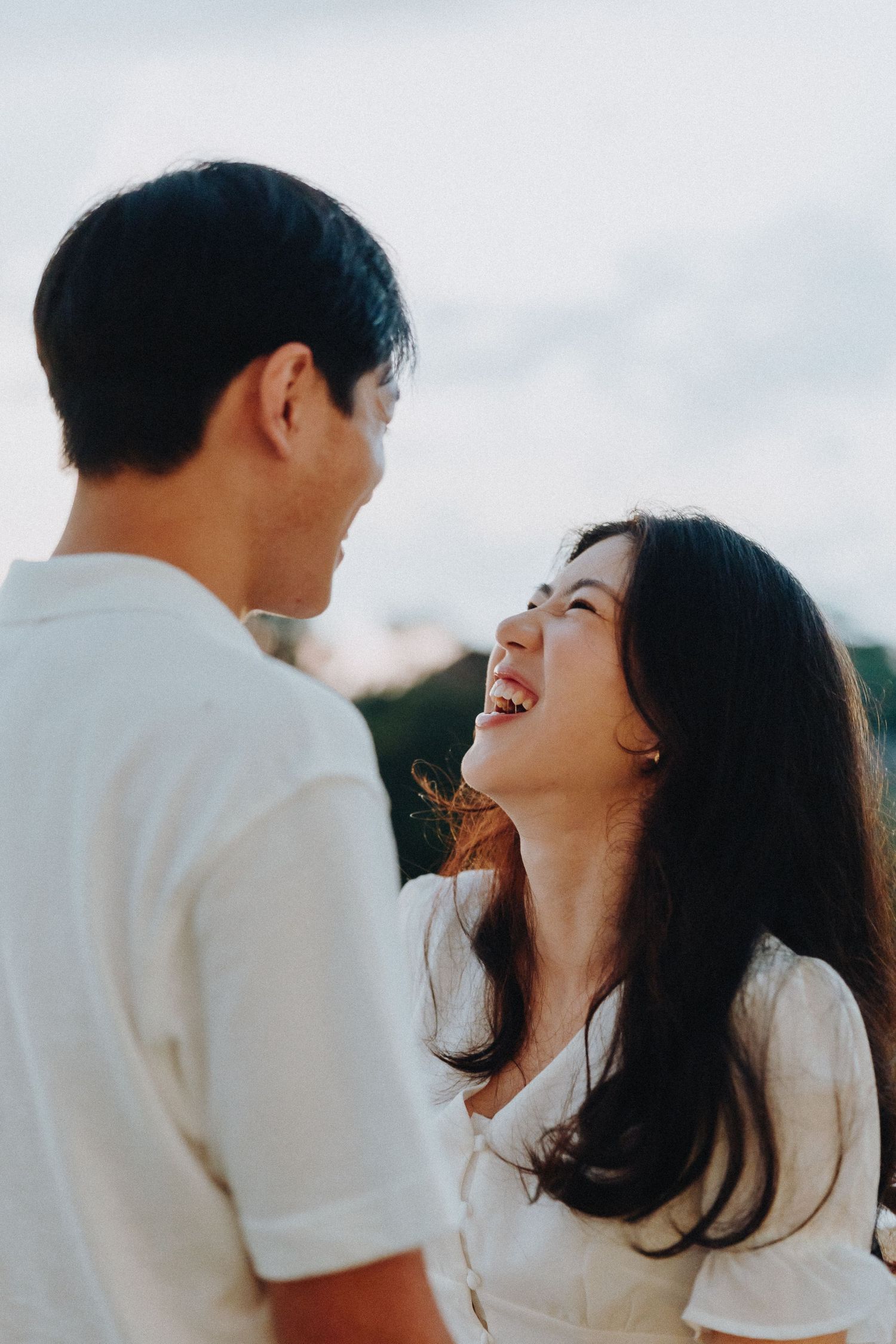 A joyful couple shares laughter while standing against a bright background.